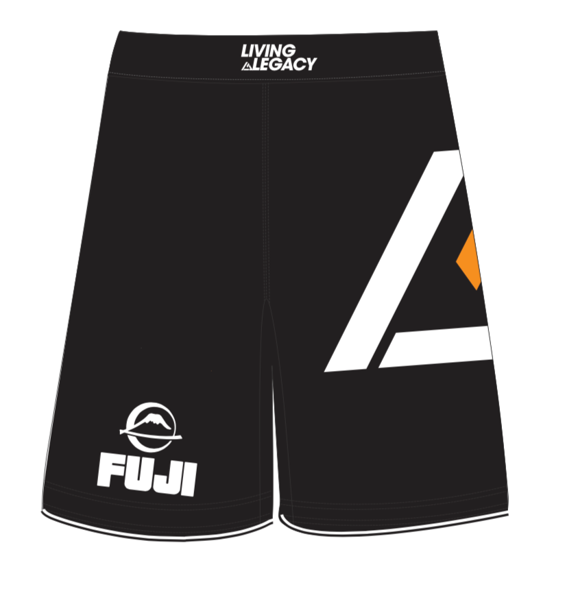 The Rilion Gracie Black Comp Team Shorts feature “LIVING LEGACY” on the waistband, “FUJI” with a mountain logo on one leg, and a bold geometric design in white and orange shapes on the other leg.
