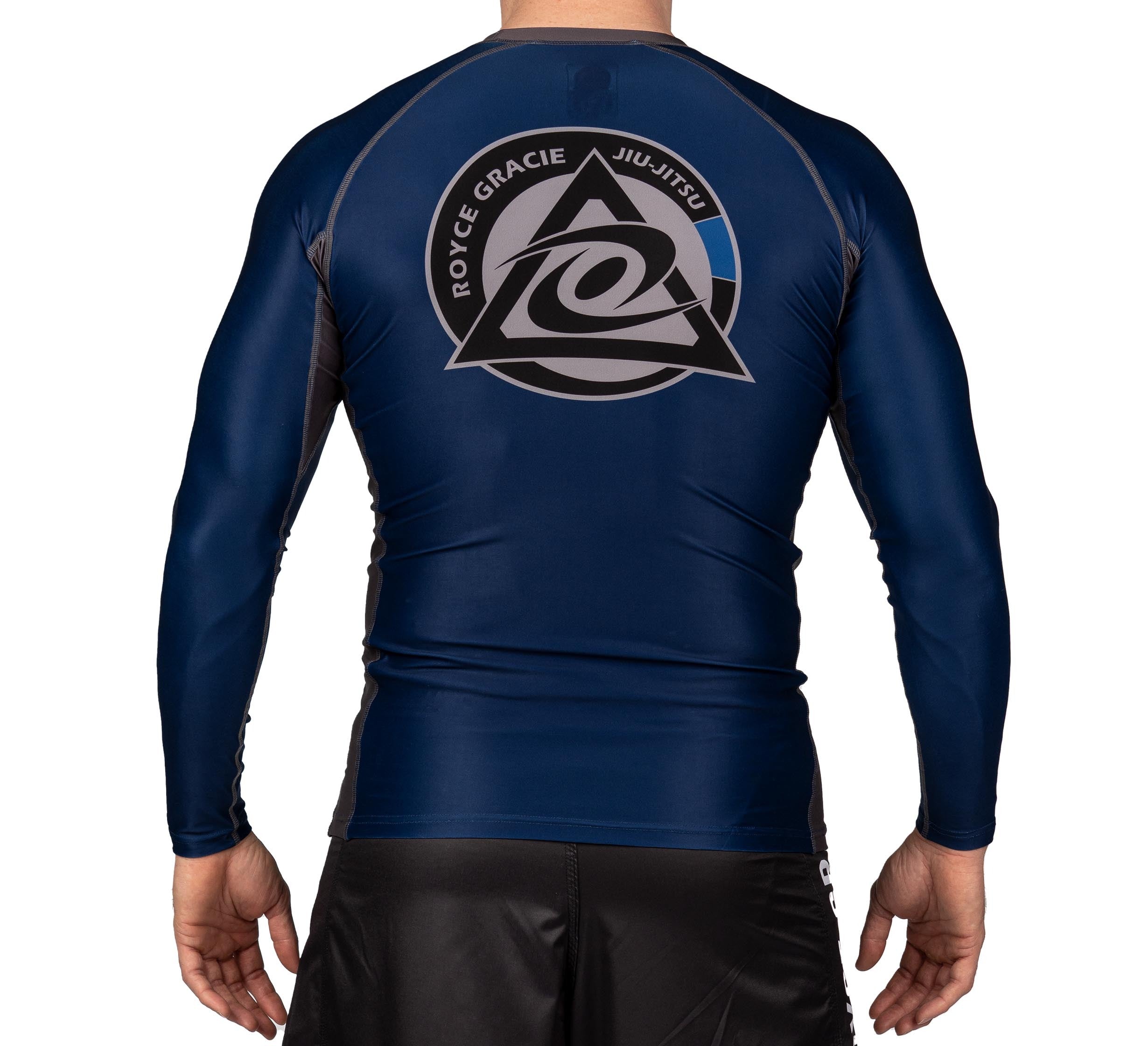 A person seen from behind wears the Royce Gracie Official Long Sleeve Rashguard in navy blue, featuring the Royce Gracie Jiu-Jitsu logo on the back, paired with black athletic shorts.