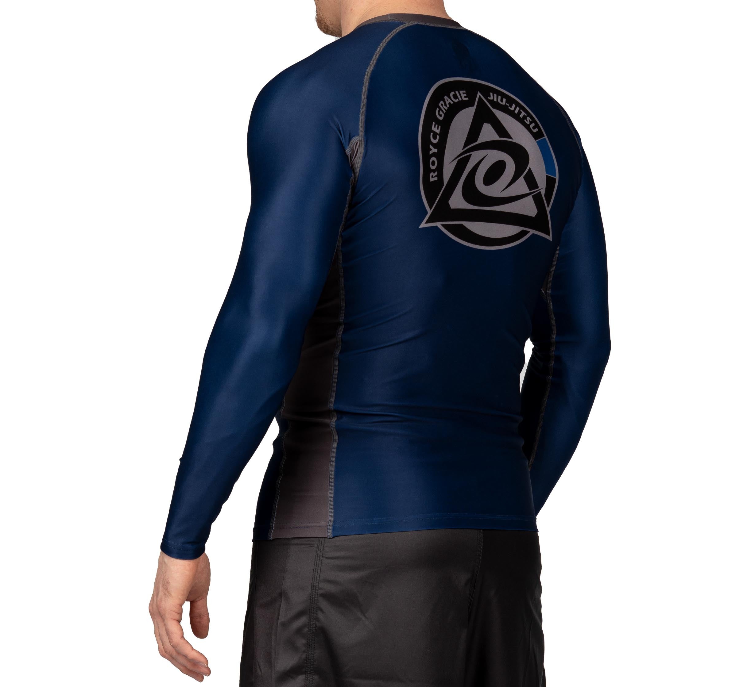 A person wears the Royce Gracie Official Long Sleeve Rashguard in navy blue and black, featuring a large Royce Gracie Jiu-Jitsu logo on the back, paired with black athletic shorts, standing against a white backdrop.