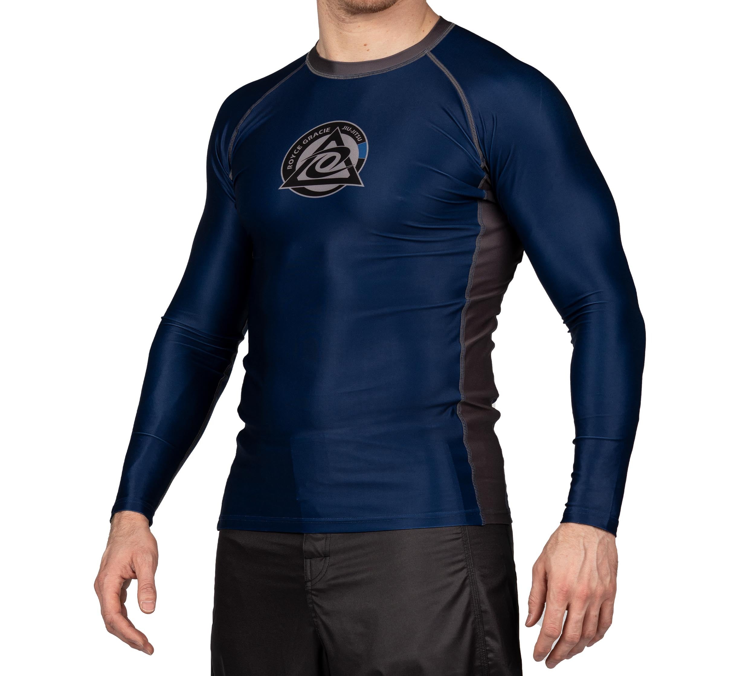 A boy wears the Royce Gracie Official Kids Long Sleeve Rashguard in navy blue and black with a chest logo, paired with black shorts, standing against a plain white background.