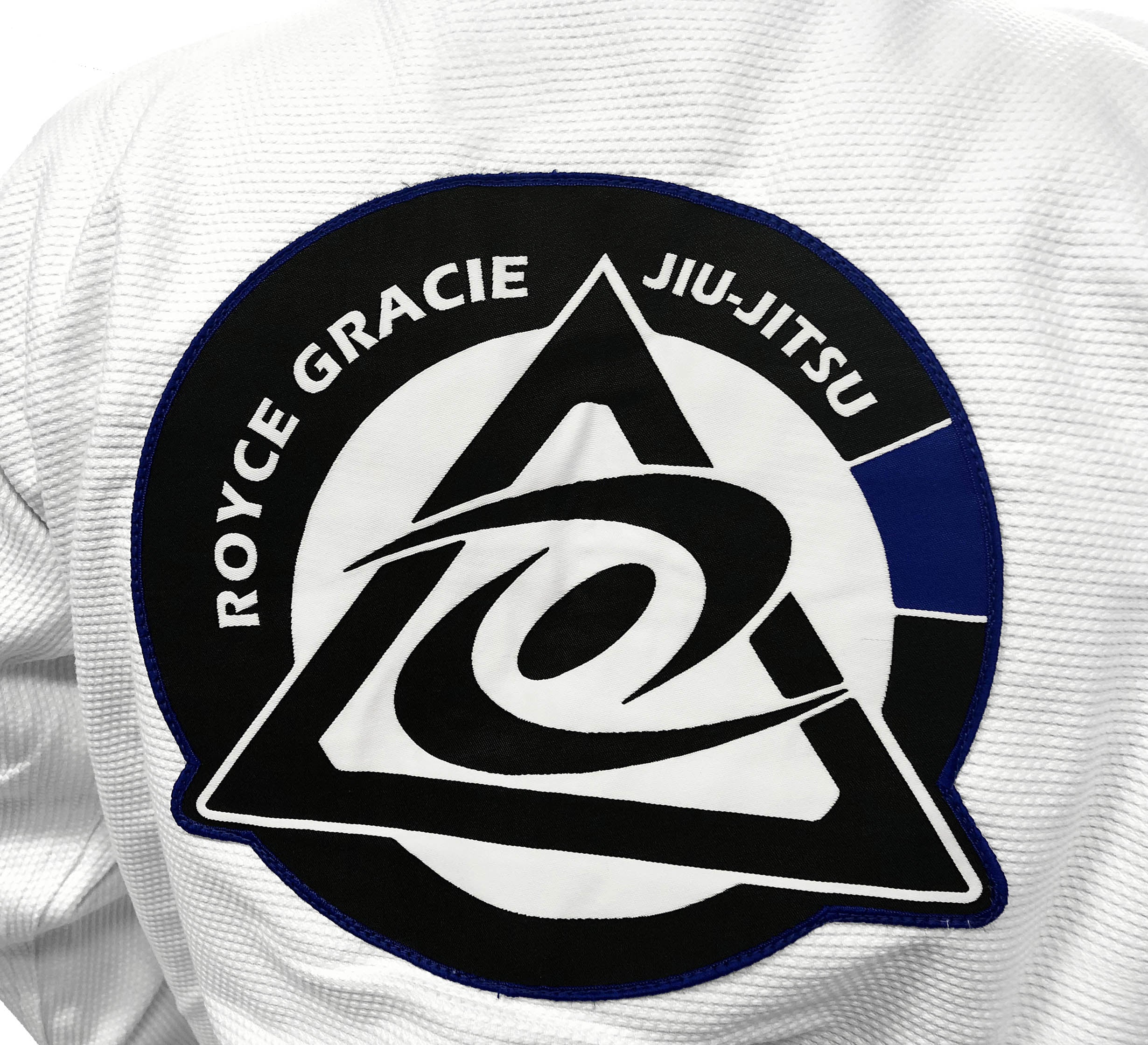 A close-up of the Royce Gracie Original Pro Series Gi’s back, featuring a prominent patch with a black triangle, stylized “G,” and circular design.