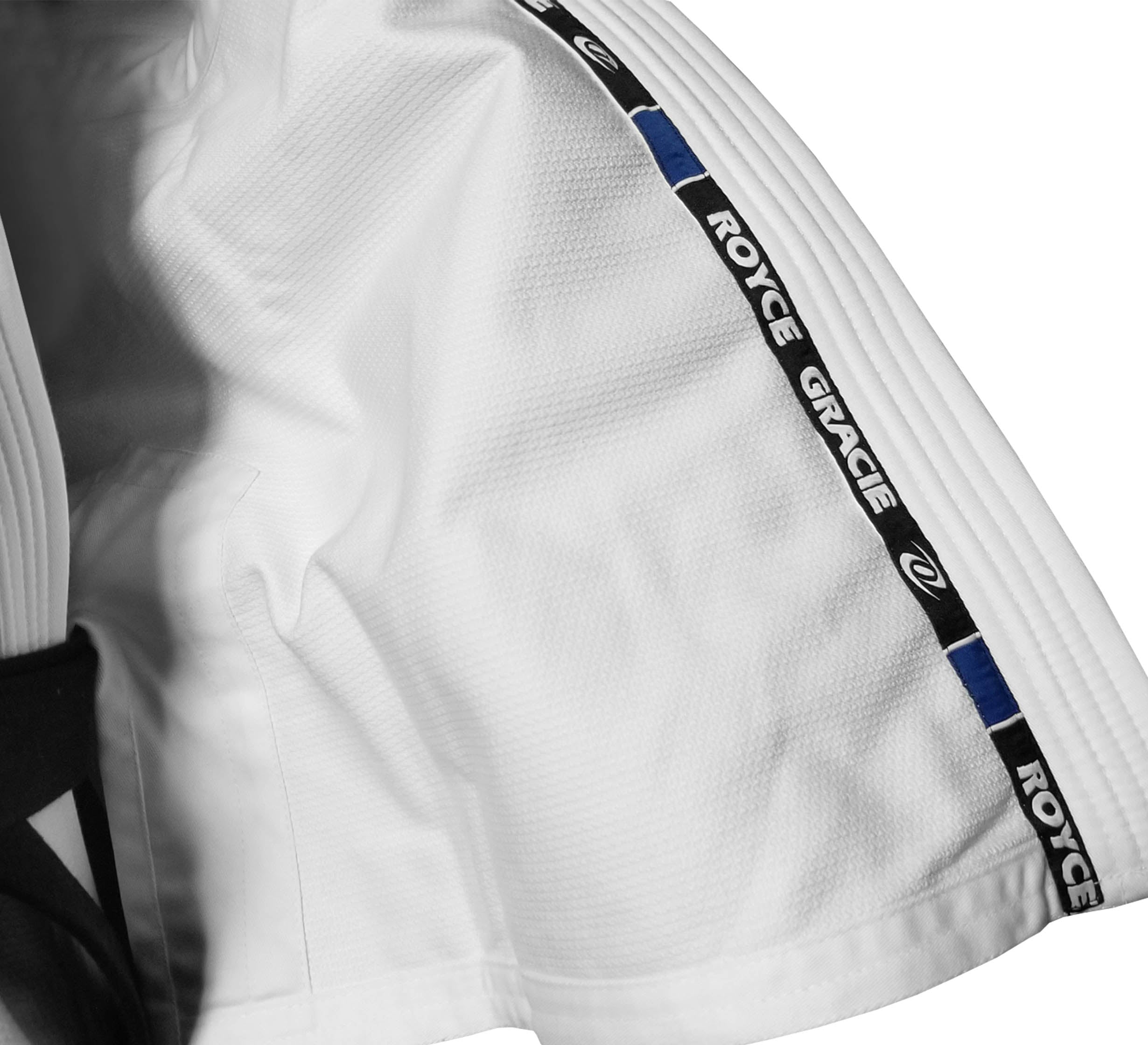 Close-up of the Official Royce Gracie Kids BJJ Gi White, showing a white martial arts gi with an inner collar strip reading ROYCE GRACIE in black and white, blue stripes, and a small logo.