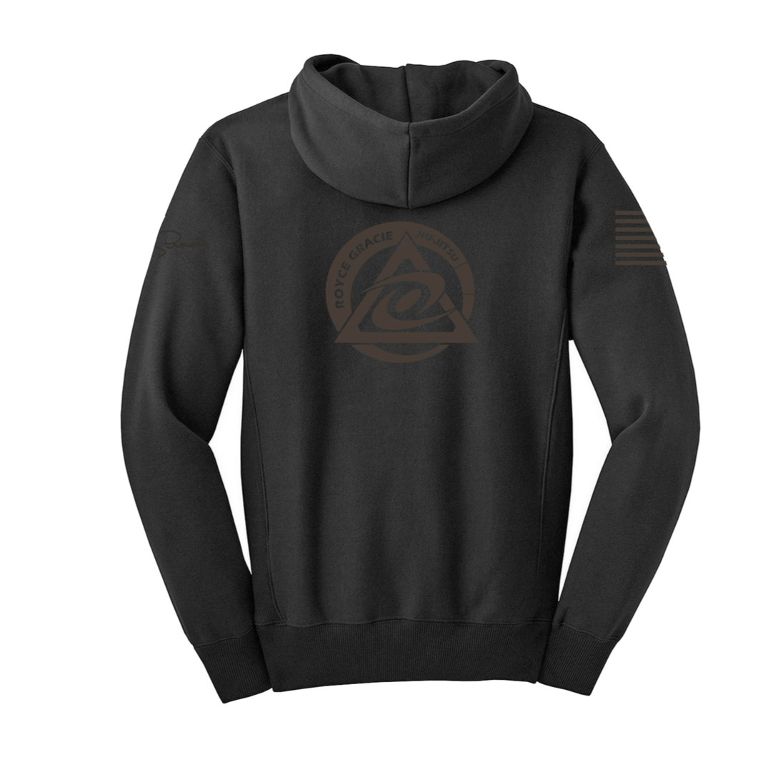 The Royce Gracie Charcoal Blackout Zip Up Hoodie YOUTH is shown from the back, featuring a large circular “Rorion Gracie Approved” logo in a triangle with an abstract center symbol, plus U.S. flag and signature graphics on the sleeves.