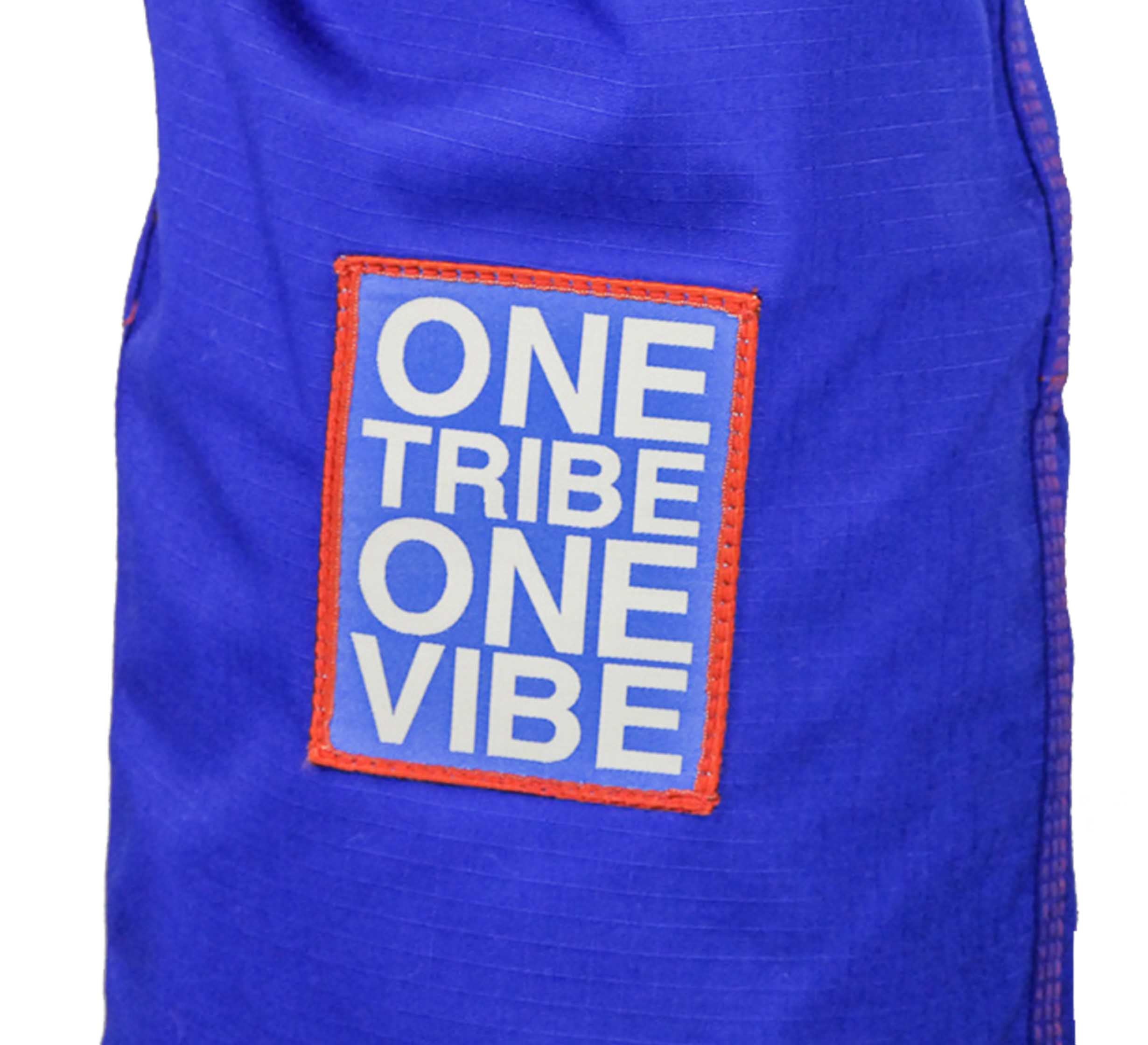 The SBG One Tribe Blue Super Lite Gi features a blue fabric with a rectangular patch outlined in red stitching and white uppercase text that reads ONE TRIBE ONE VIBE.