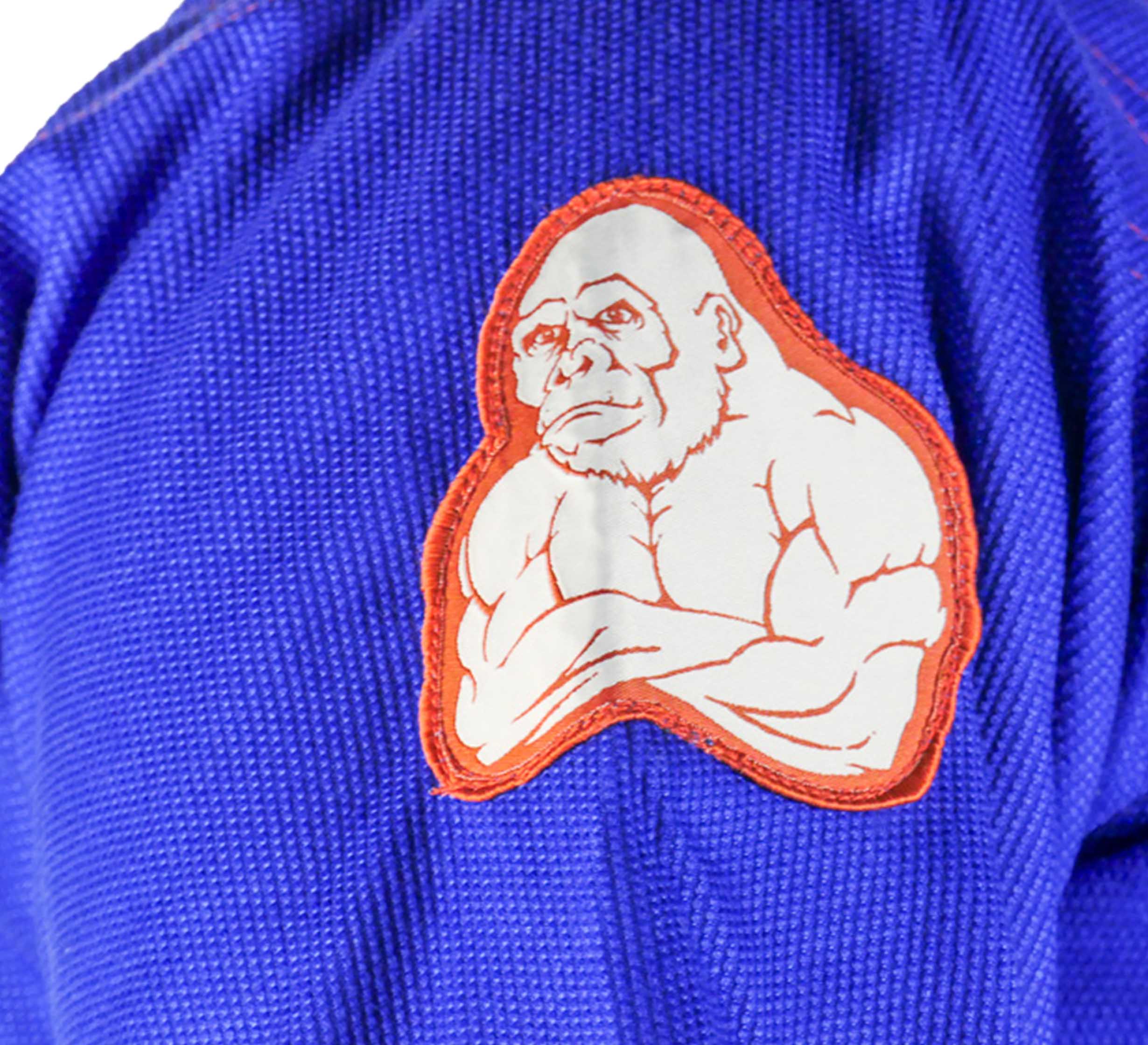 A close-up of the SBG One Tribe Blue Super Lite Gi shows its textured blue fabric and a patch featuring a cartoon gorilla with muscular, crossed arms outlined in orange.