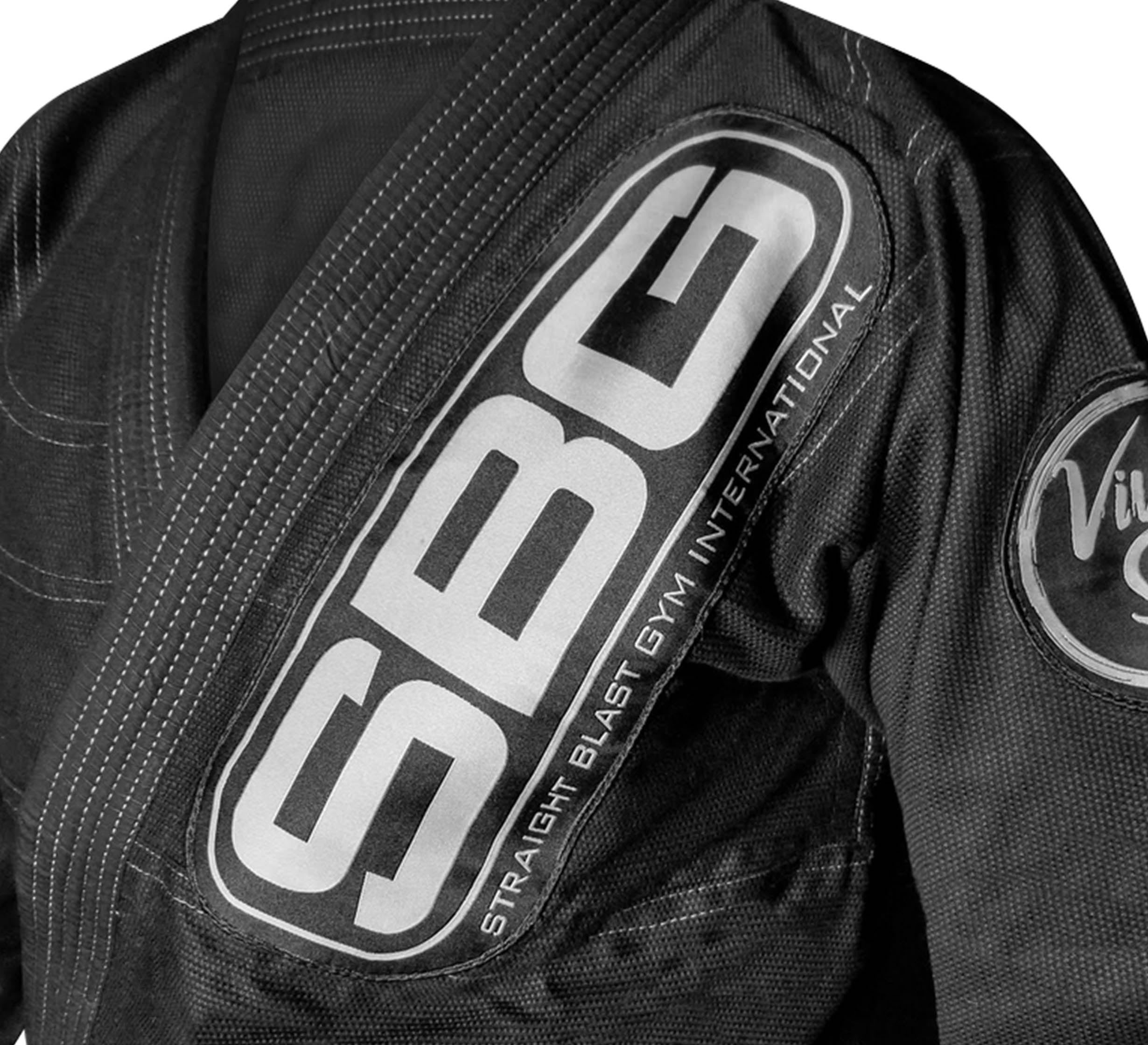 Close-up of the SBG Super Lite Womens Gi in black, featuring a large SBG patch and "Straight Blast Gym International" on the chest, plus a circular sleeve patch. Shown on a white background.