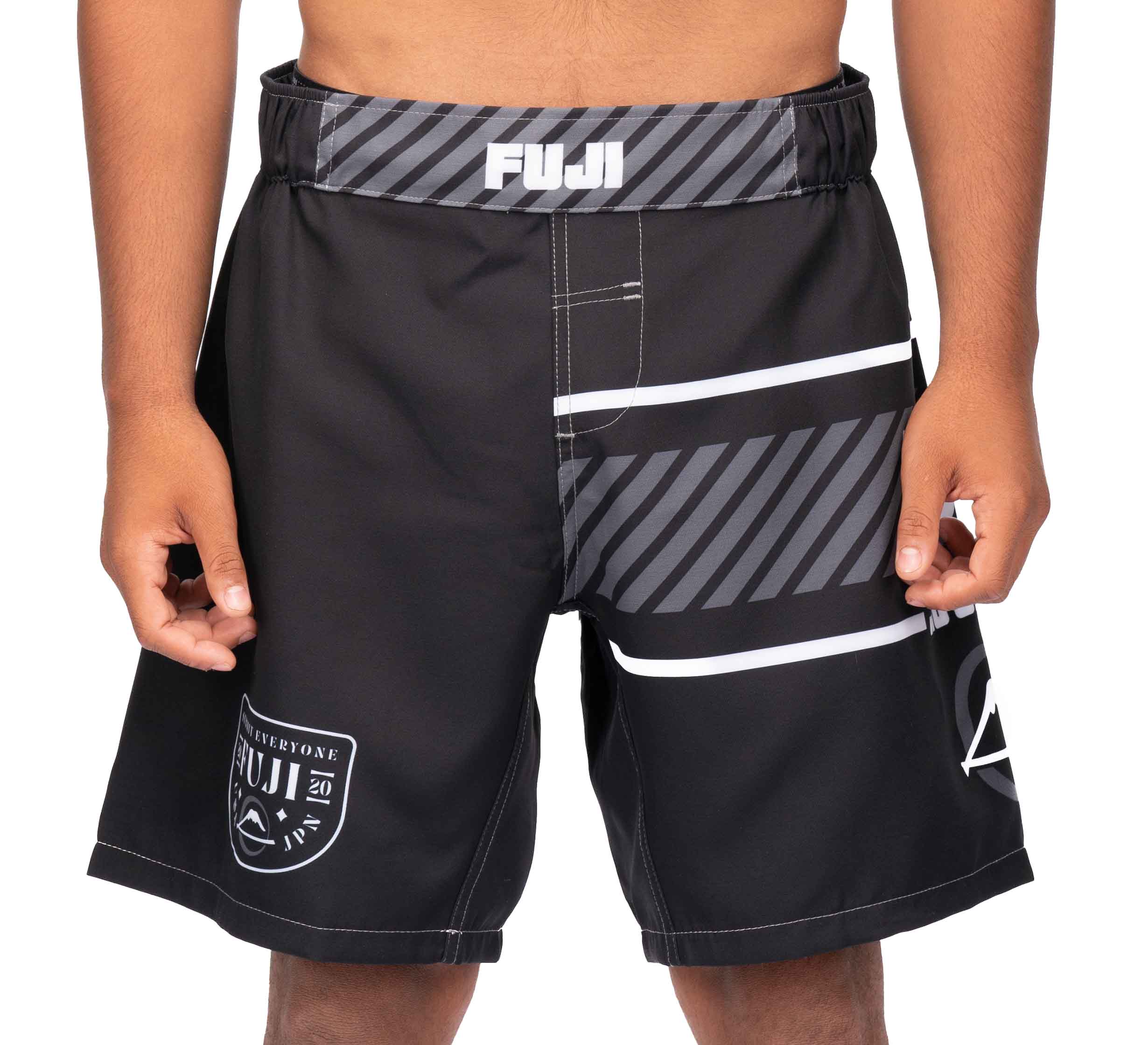 A person wears black Freestyle 2.0 Ranked Grappling Shorts featuring gray and white geometric designs, standing with hands by their sides. Visible logos and branding appear on the waistband and left leg.