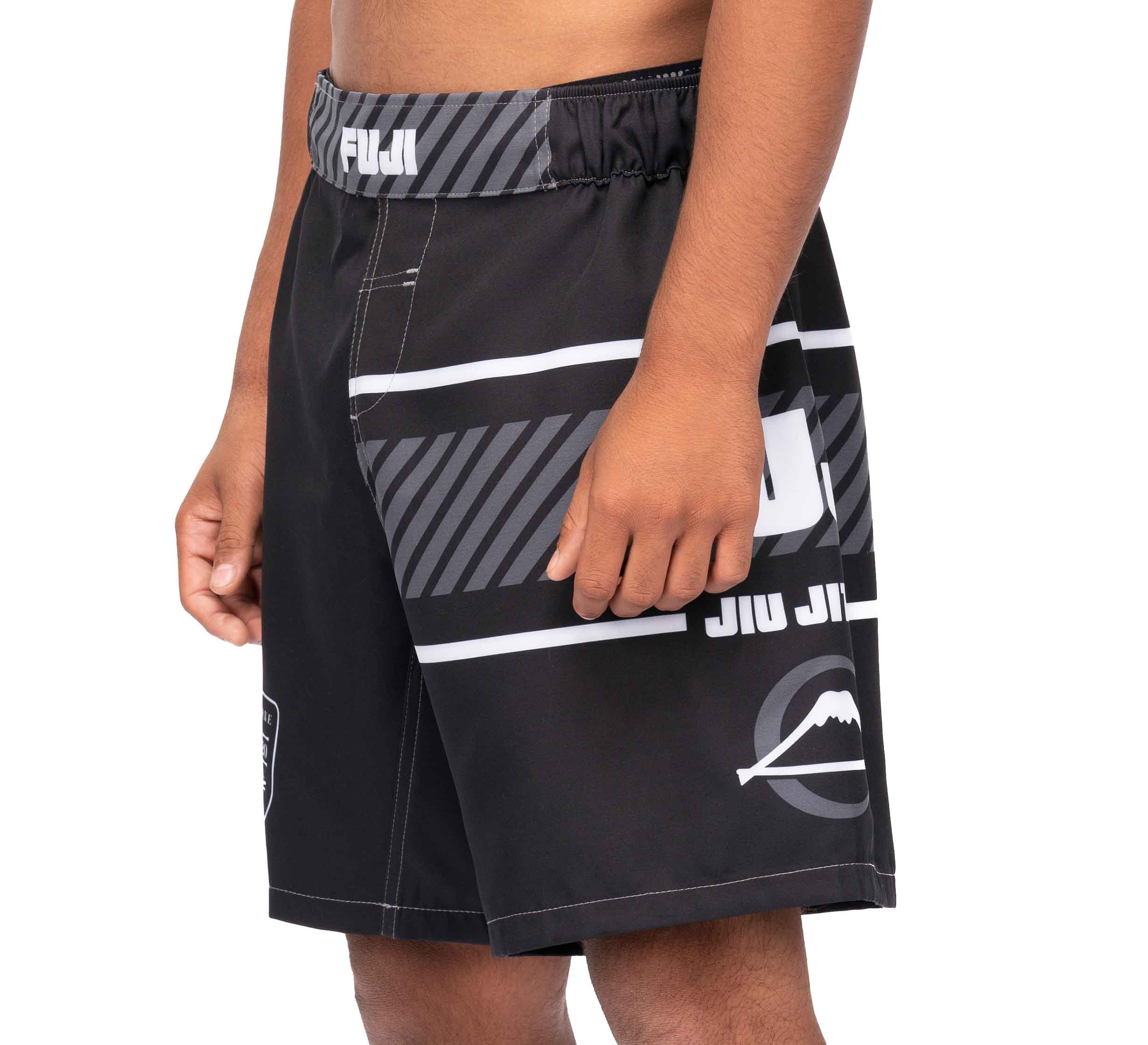A person wearing Freestyle 2.0 Ranked Grappling Shorts in black and gray with white accents, geometric patterns, "JIU JITSU" text, a mountain logo on the left leg, and an elastic waistband.