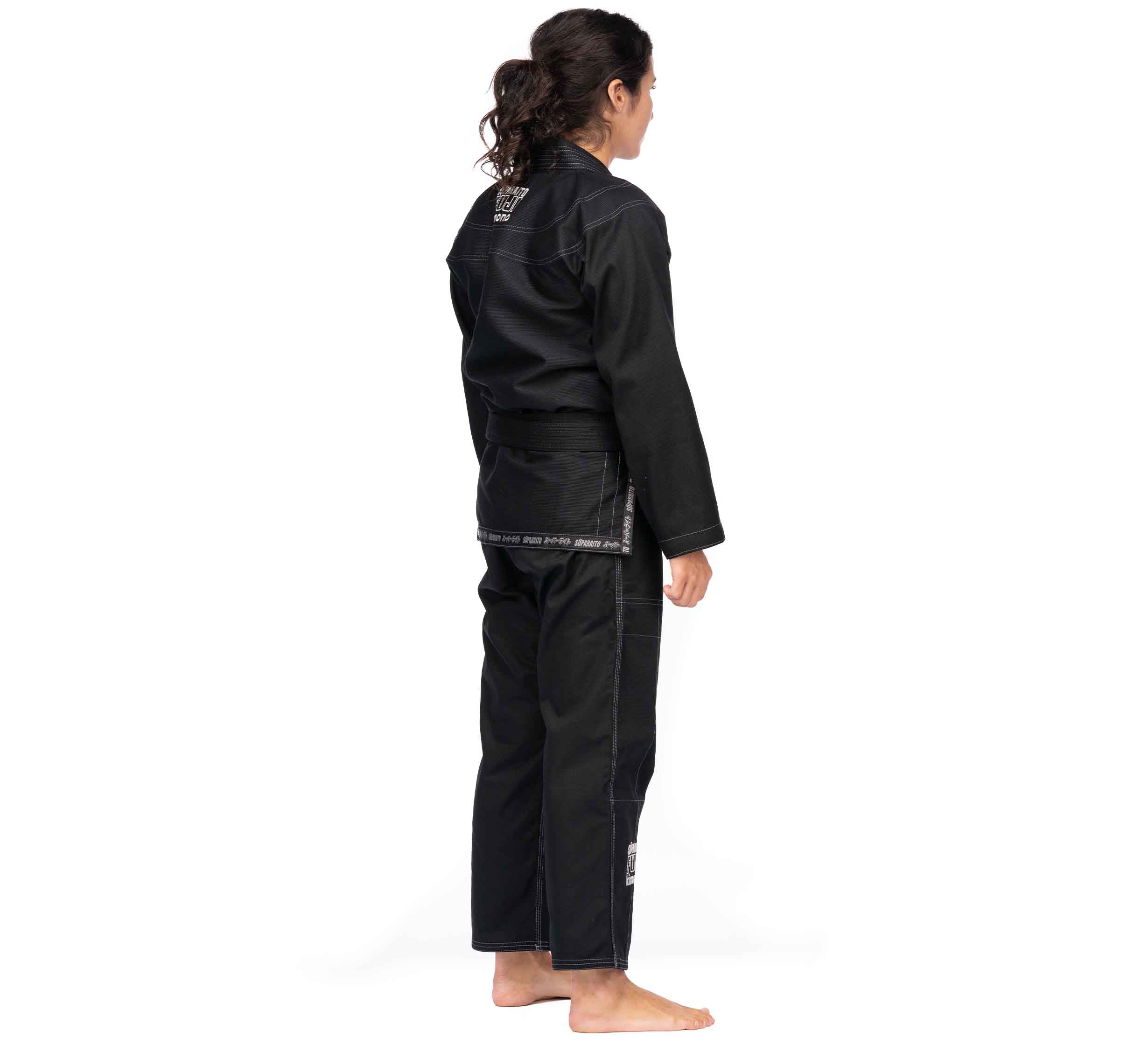 A person with long, dark hair in a ponytail is standing barefoot and facing away, wearing the Suparaito BJJ Gi (Unisex Size) Black with a black belt, set against a plain white background.