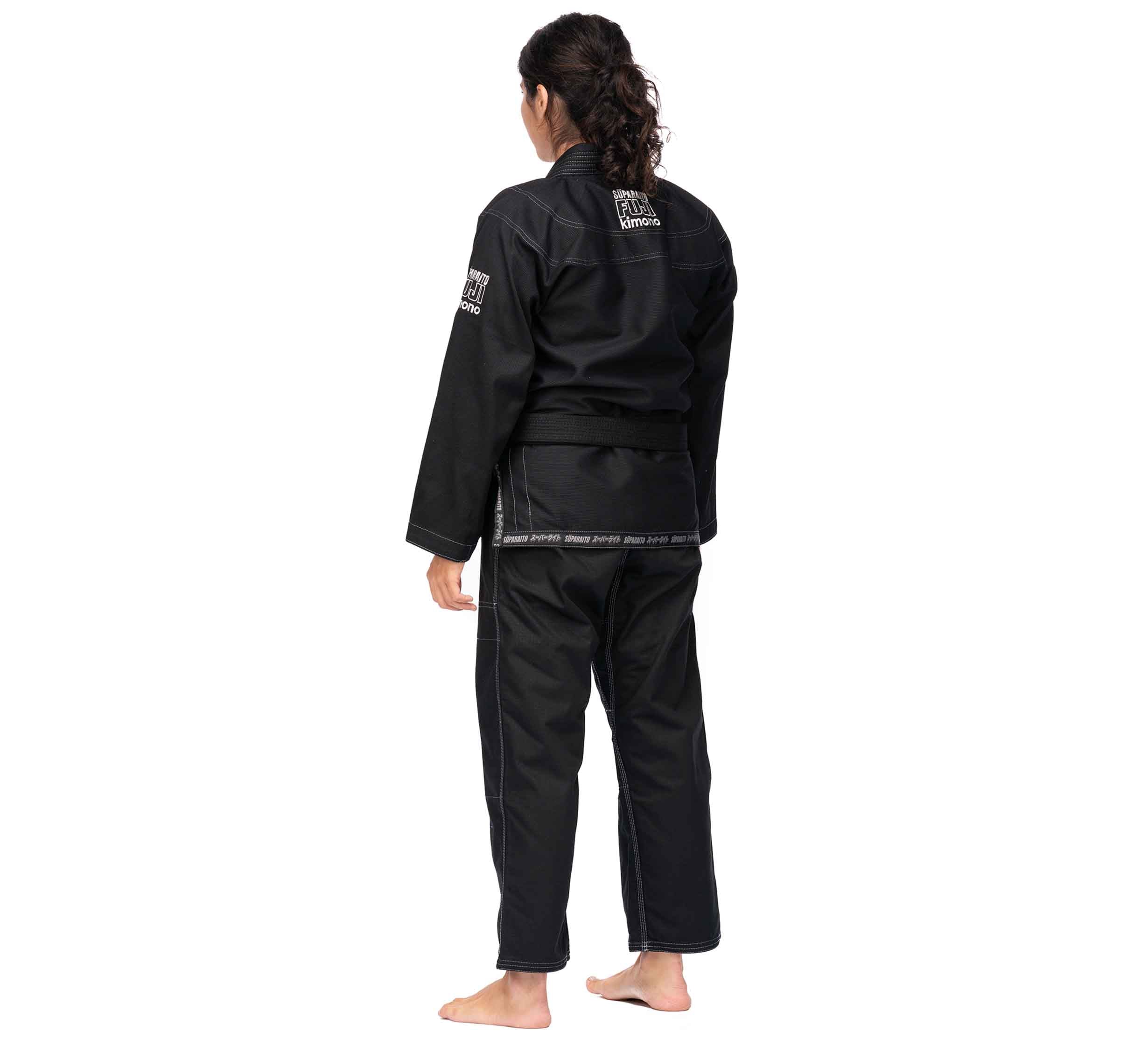 A person stands barefoot, facing away, wearing the Suparaito BJJ Gi (Unisex Size) in black with a belt. The gi features white stitching and patches on the back and sleeves. The background is plain white.