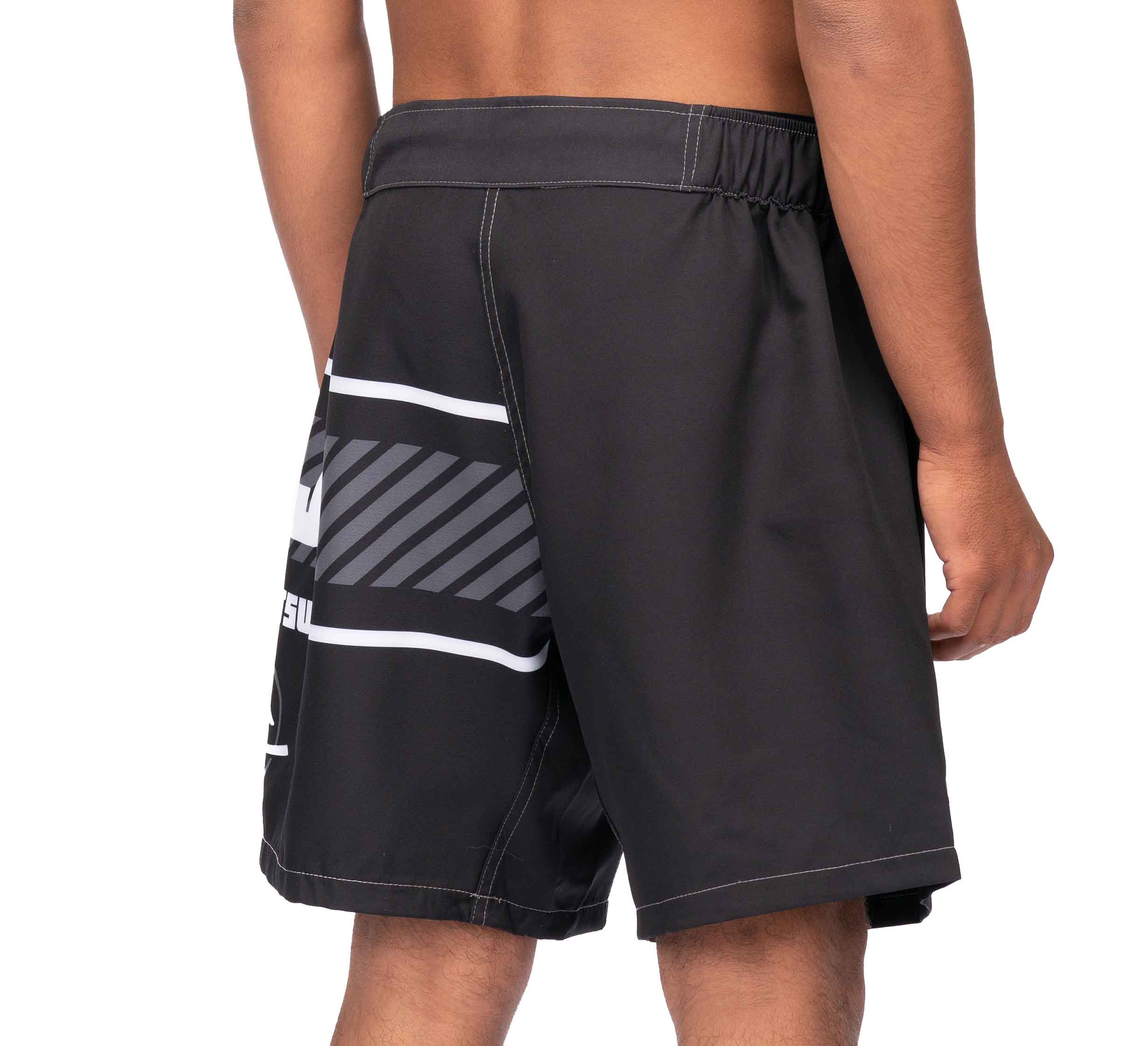 A person wearing Freestyle 2.0 Ranked Grappling Shorts with a black base and a white and gray graphic design on the side, standing with their back and right arm visible.