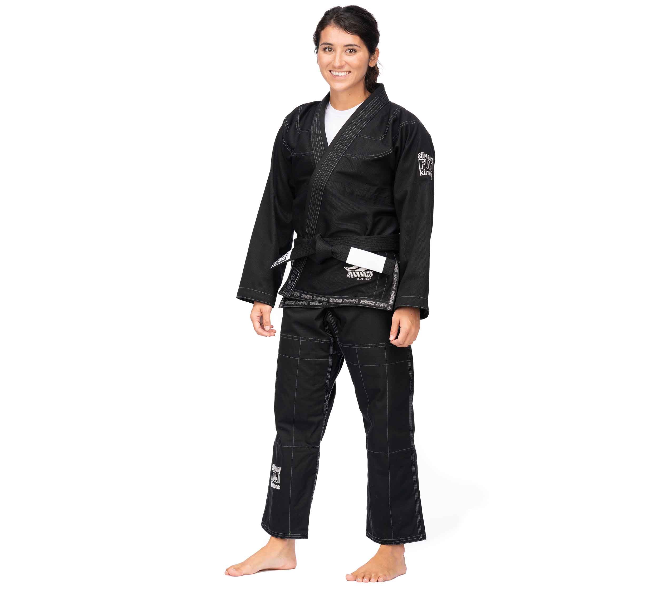 A person wearing the Suparaito BJJ Gi (Unisex Size) Black with a white belt, barefoot and smiling, stands against a plain white background.