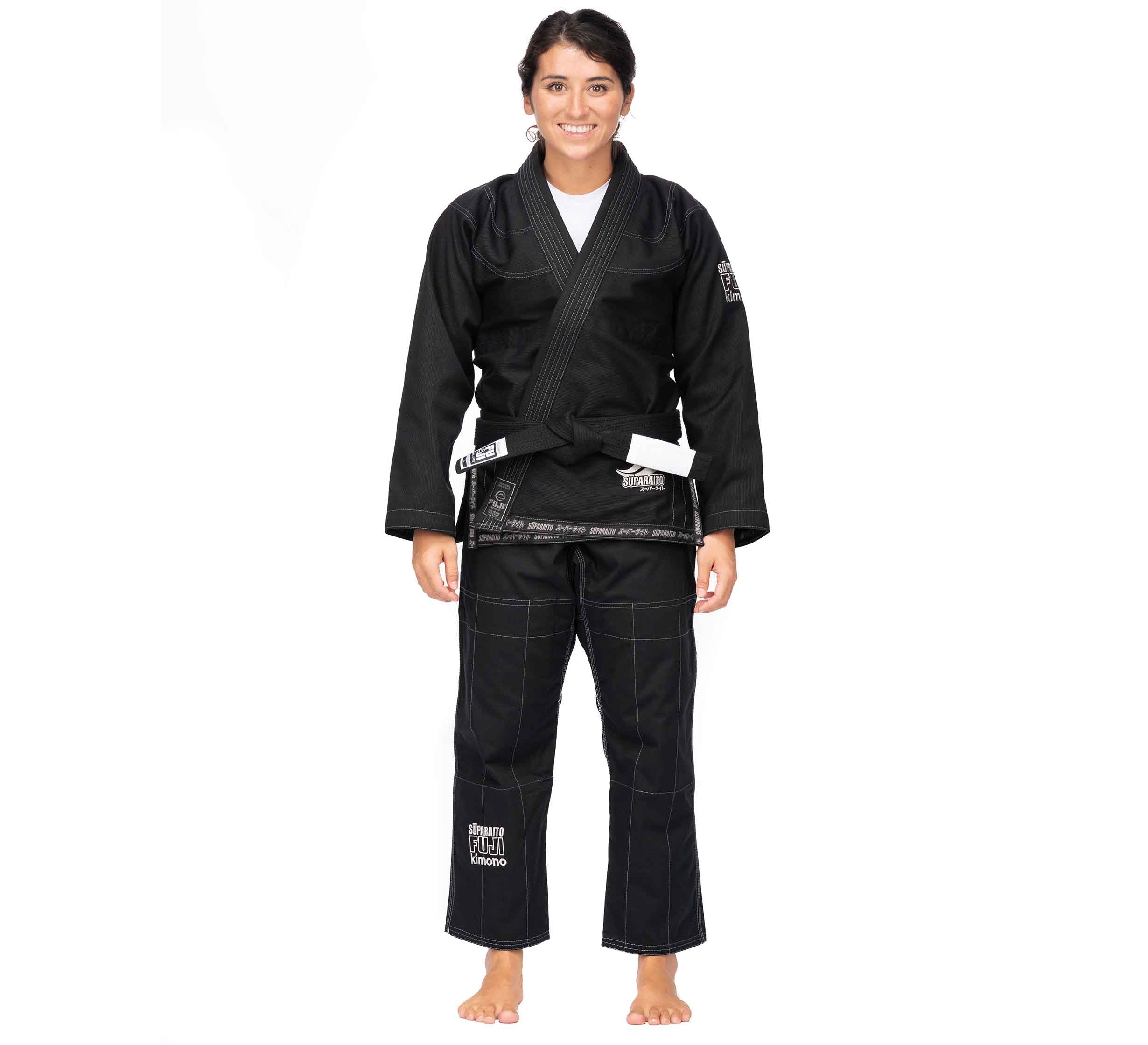 A person stands barefoot, smiling, and wearing the Suparaito BJJ Gi (Unisex Size) in black with a white belt against a plain white background.