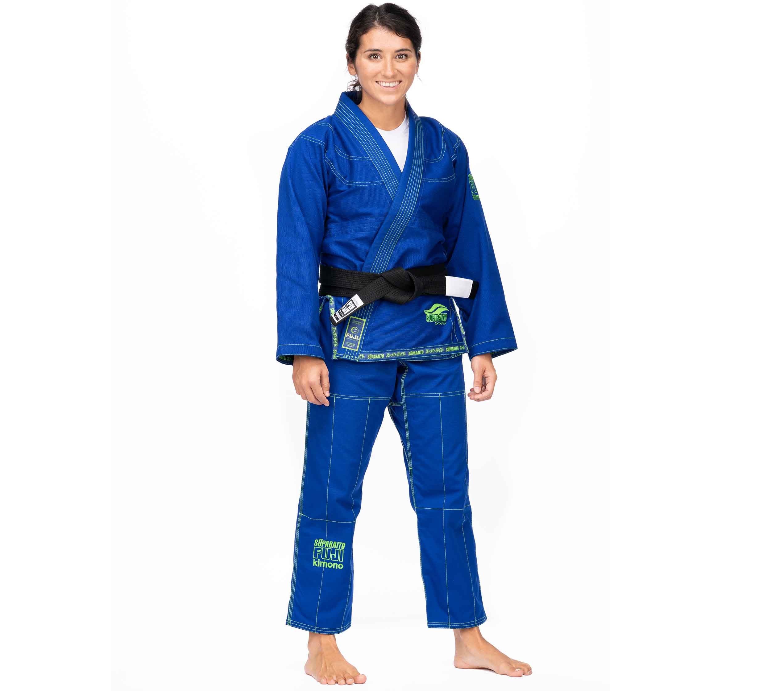 A woman smiles barefoot in the Suparaito BJJ Gi (Unisex Size) Blue with a black belt, standing against a plain white background.