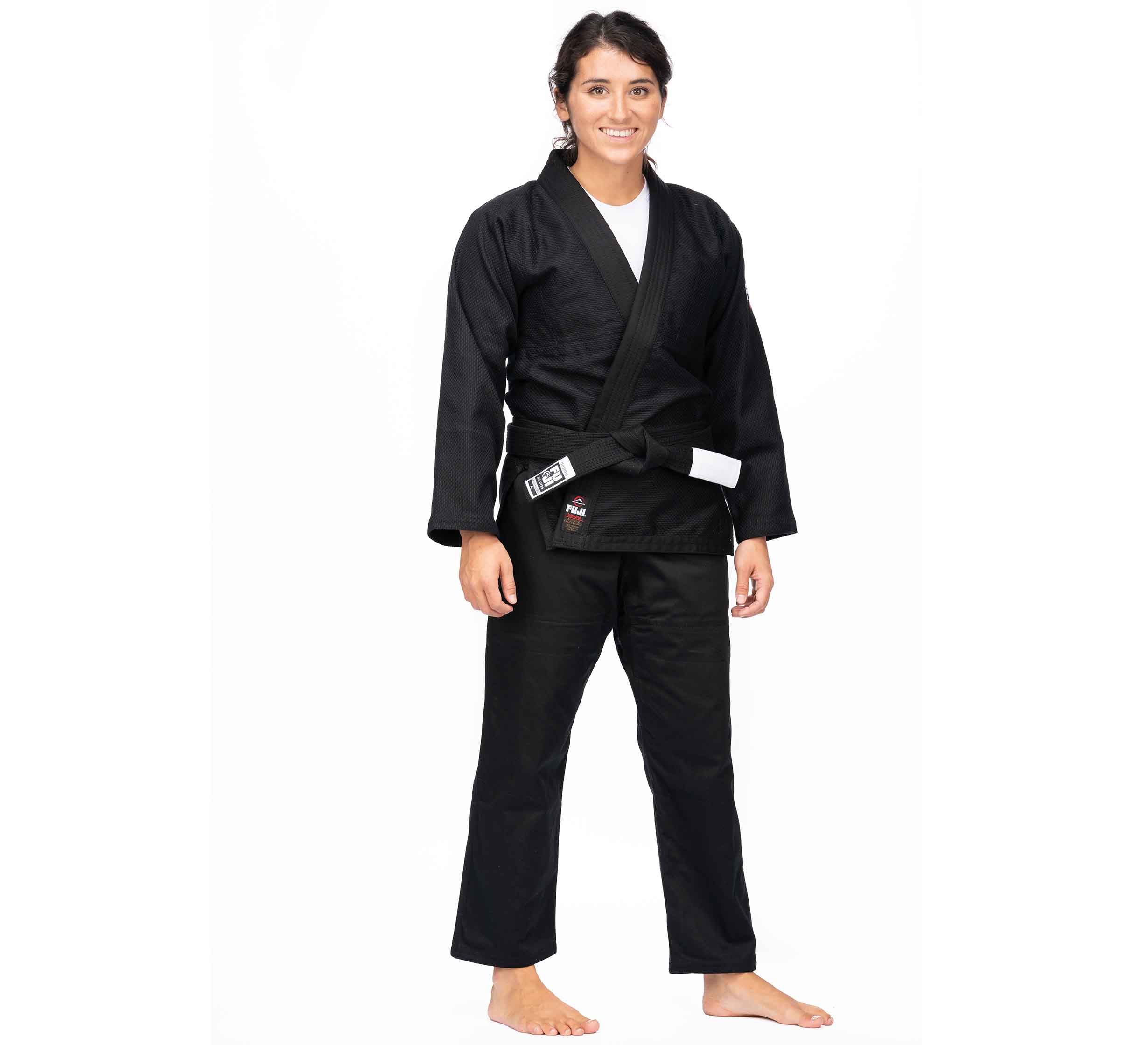 A person stands barefoot on a white background, smiling and wearing the All Around BJJ Gi Black (Unisex Size) with a black belt.