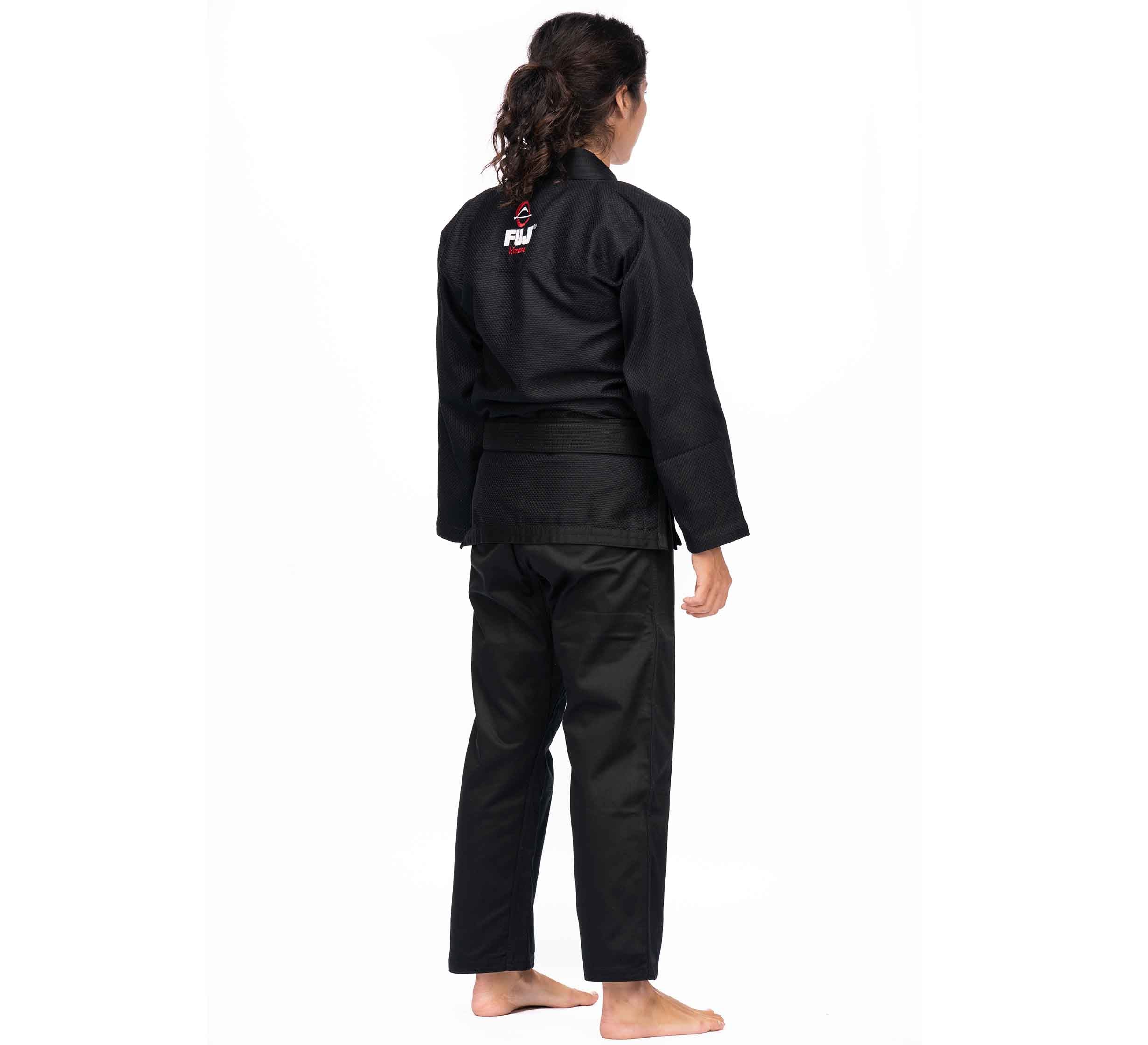A person with long, dark hair in a ponytail stands barefoot, facing away and wearing the All Around BJJ Gi Black (Unisex Size) with a belt. The gi features a red and white logo on the upper back.