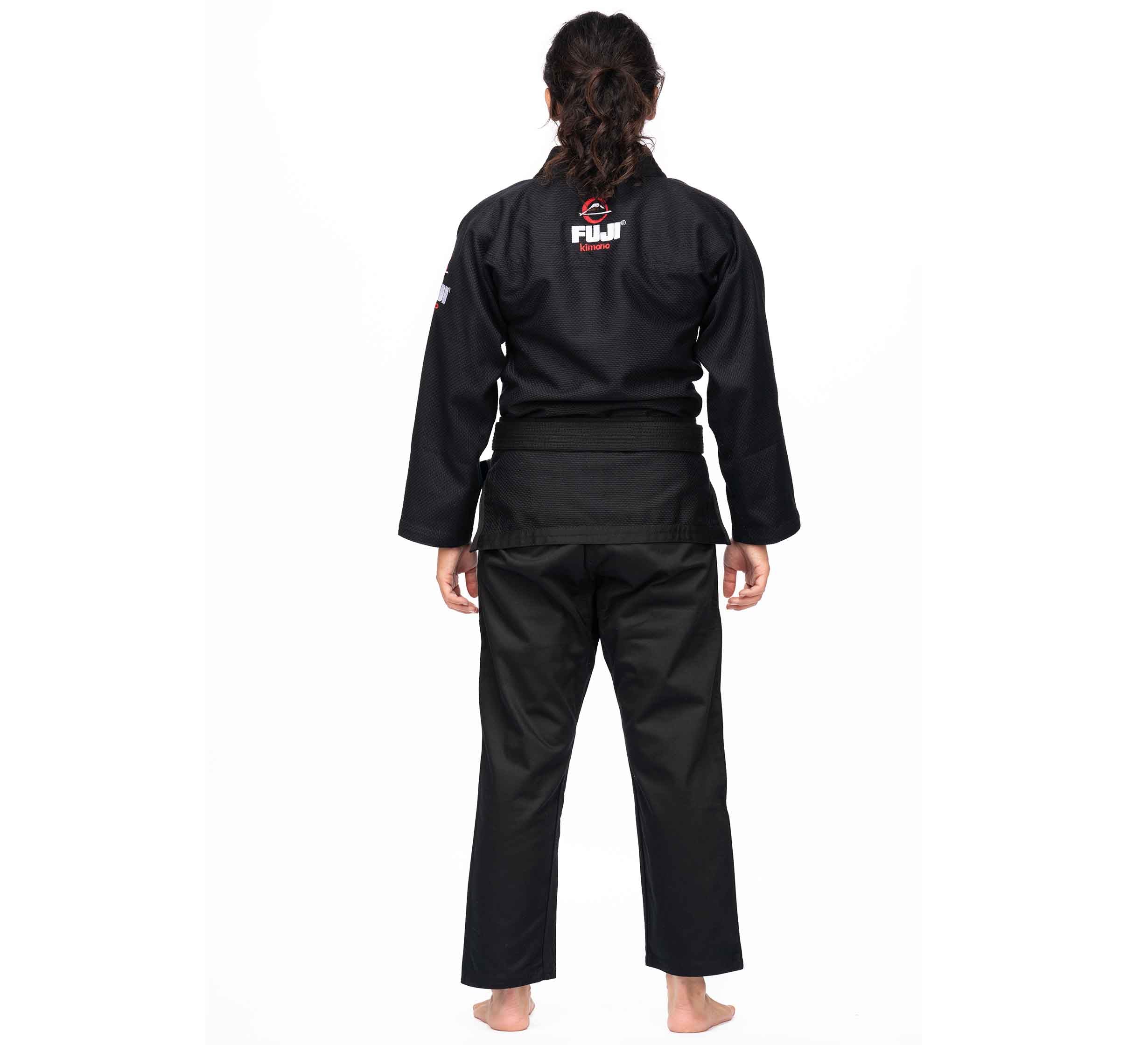 A person with long hair, barefoot and facing away on a white background, wears the All Around BJJ Gi Black (Unisex Size) with a visible FUJI logo on the back.