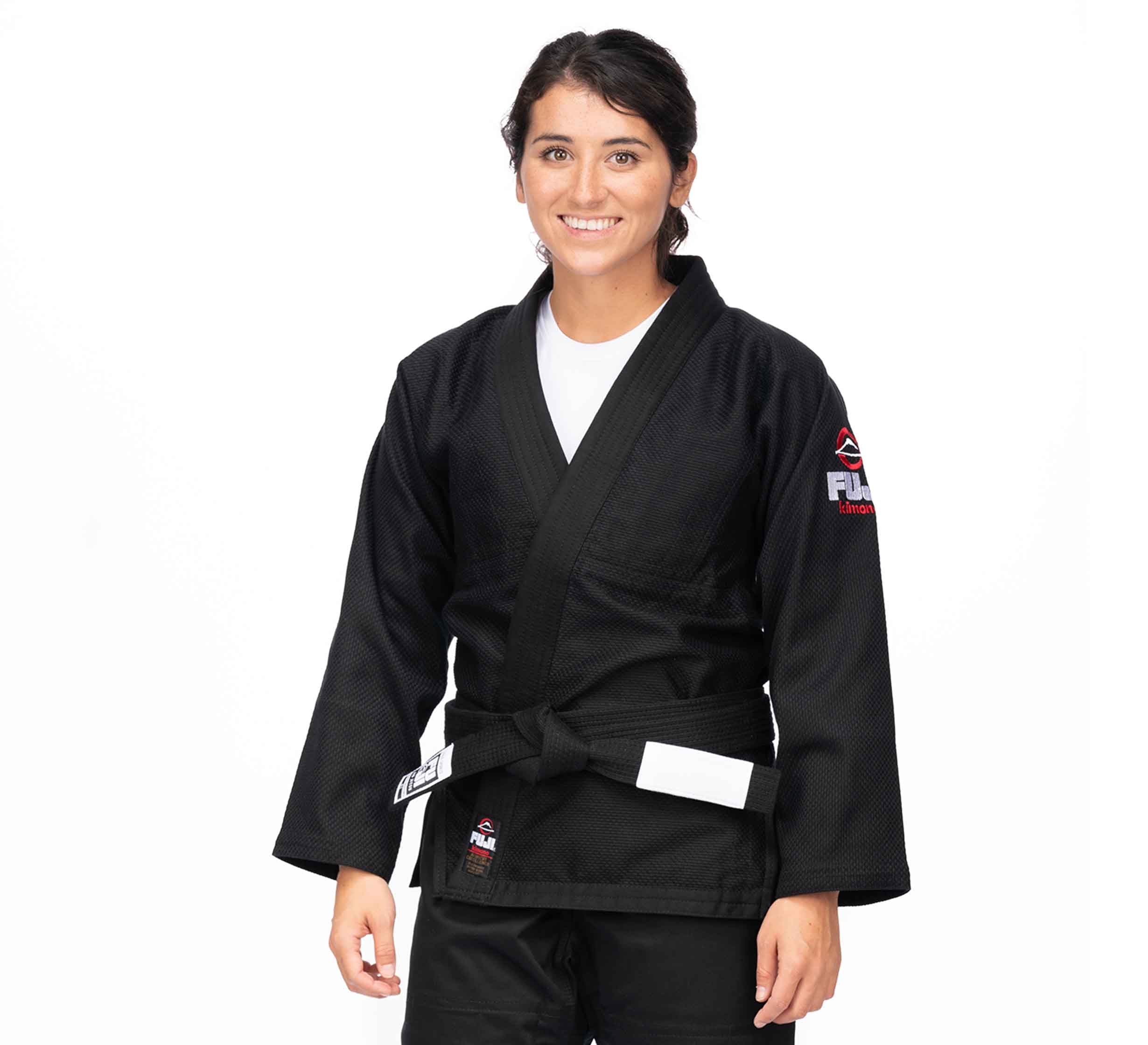A woman smiles against a plain white background wearing the All Around BJJ Gi Black (Unisex Size) with a white belt and patches on the sleeve and waist.