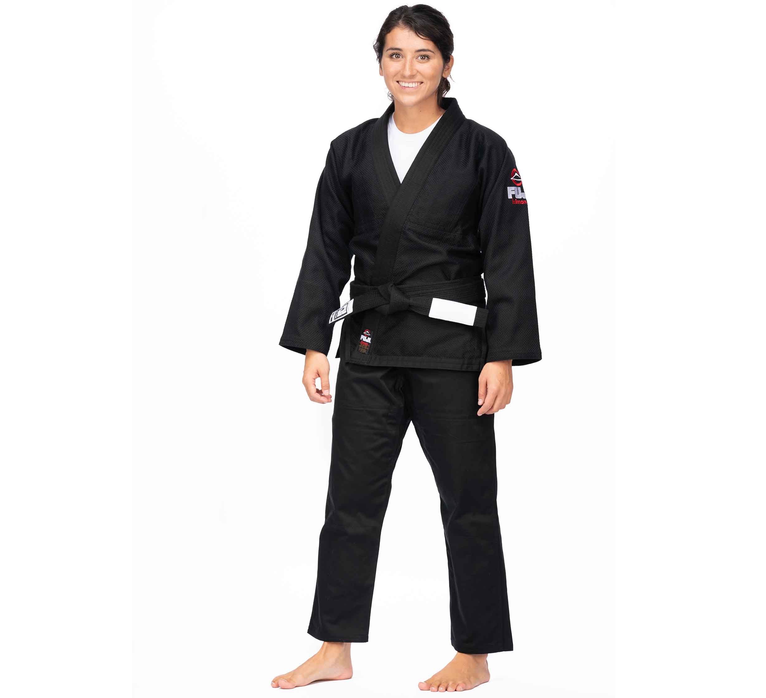 A person stands barefoot, smiling, and wearing the All Around BJJ Gi Black (Unisex Size) with a white belt against a plain white background.