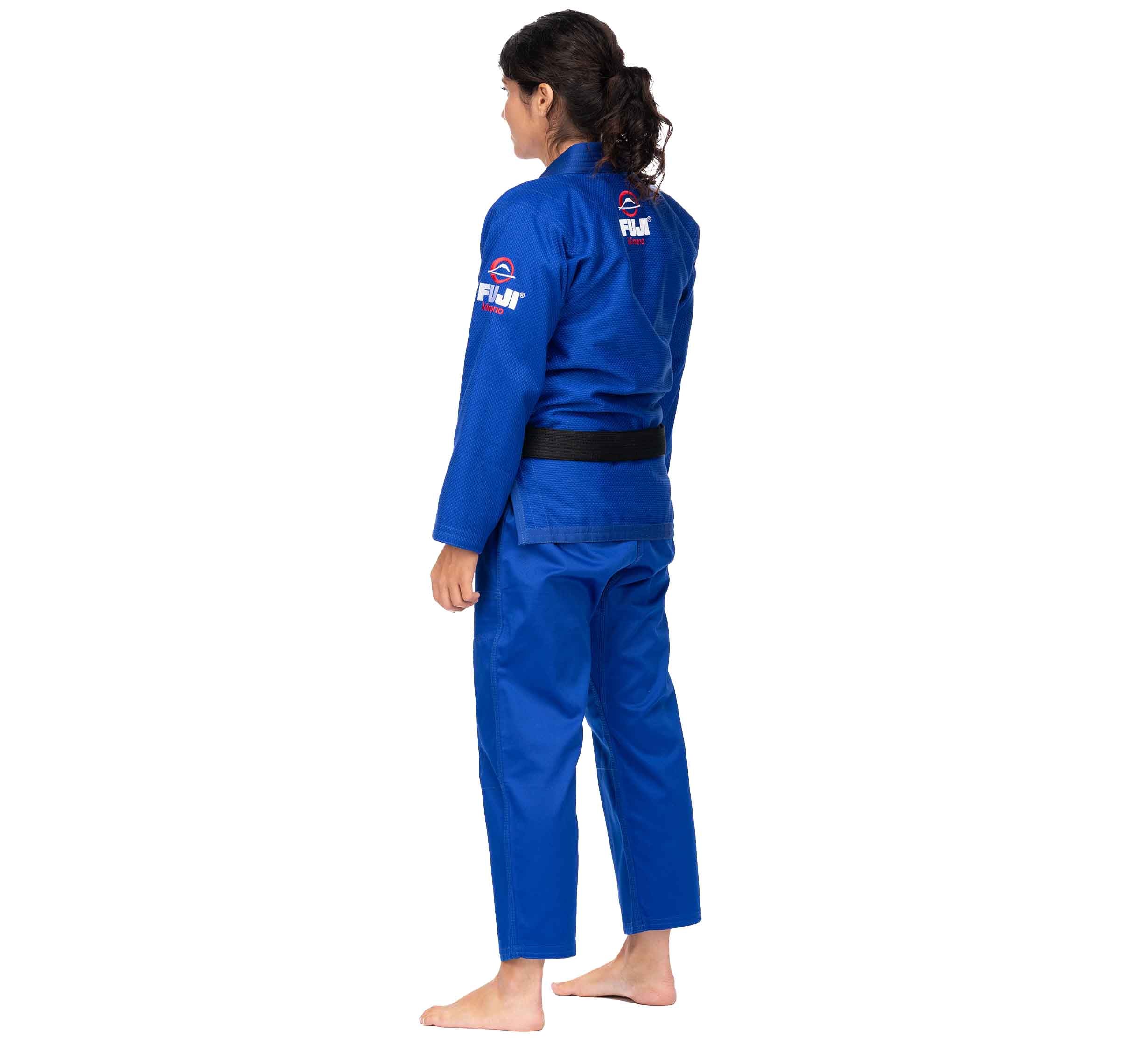 A person stands barefoot facing away, wearing the All Around BJJ Gi Blue (Unisex Size) with a black belt. Fuji logos are visible on the gi's back and sleeve. The background is plain white.