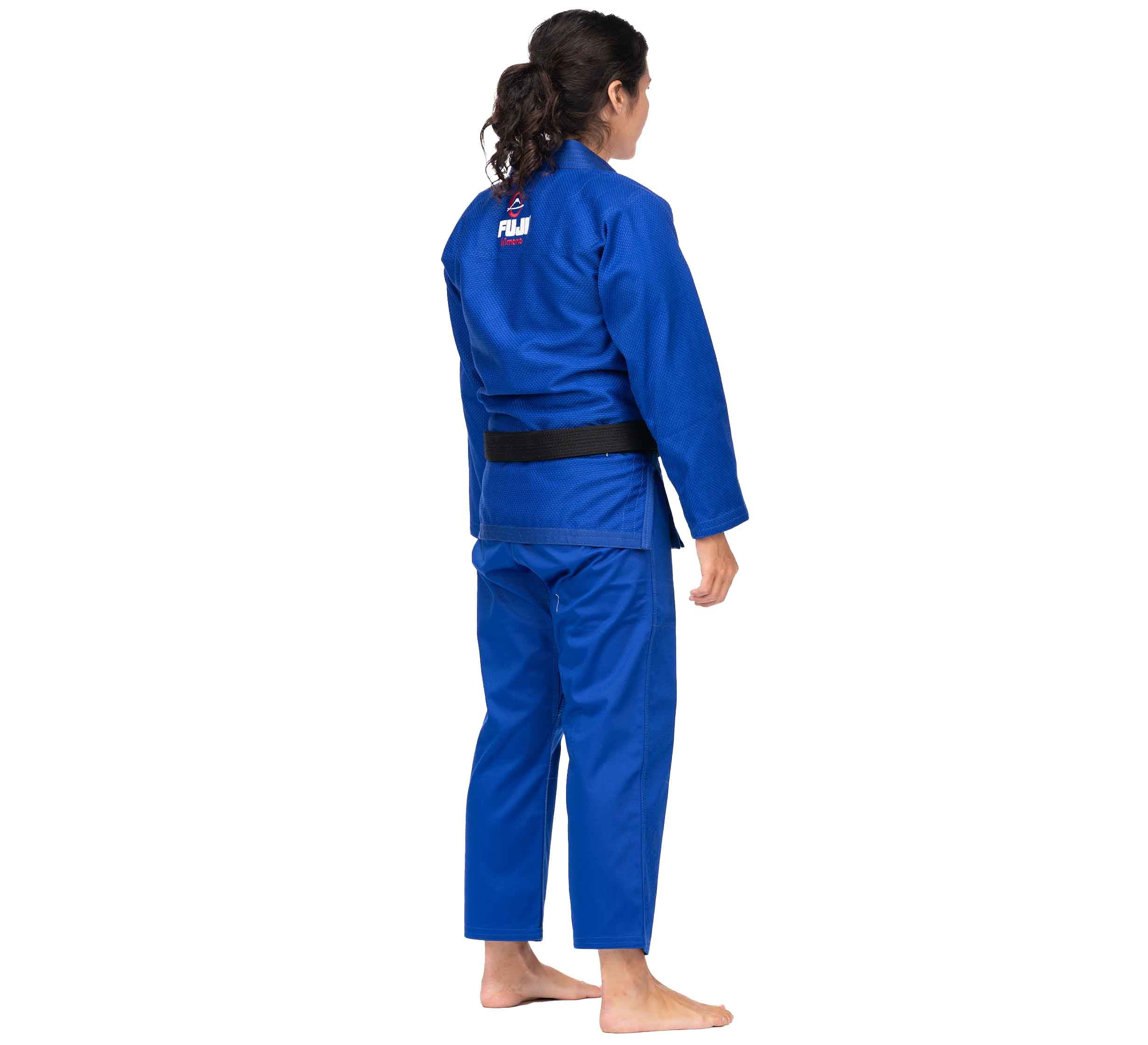 A barefoot person with long dark hair in a ponytail stands facing away, wearing the All Around BJJ Gi Blue (Unisex Size) with a black belt and logo on the upper back. The background is white.