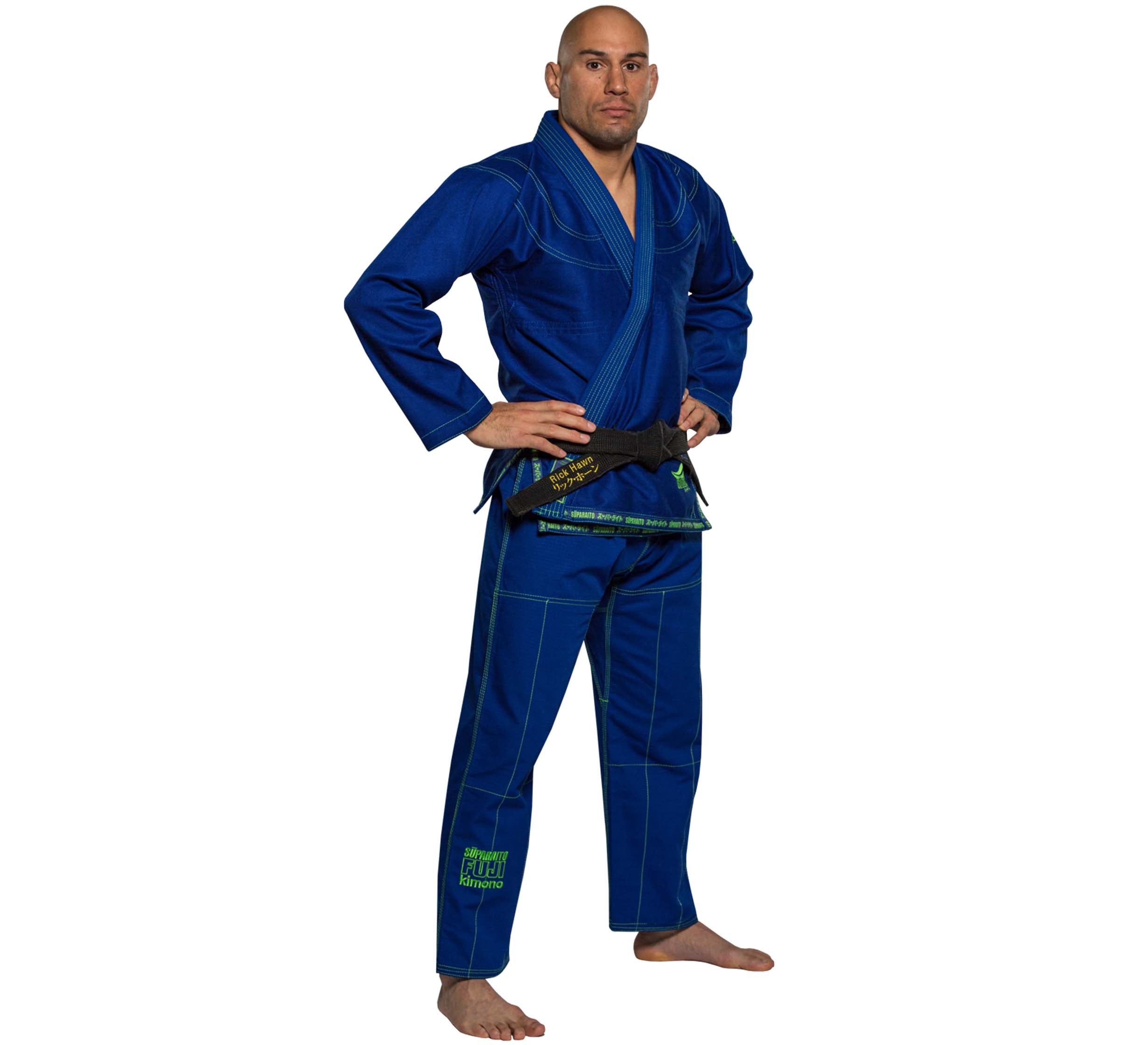 A bald man wearing the Suparaito BJJ Gi in blue with a black belt stands barefoot, facing forward, hands on hips, against a white background.