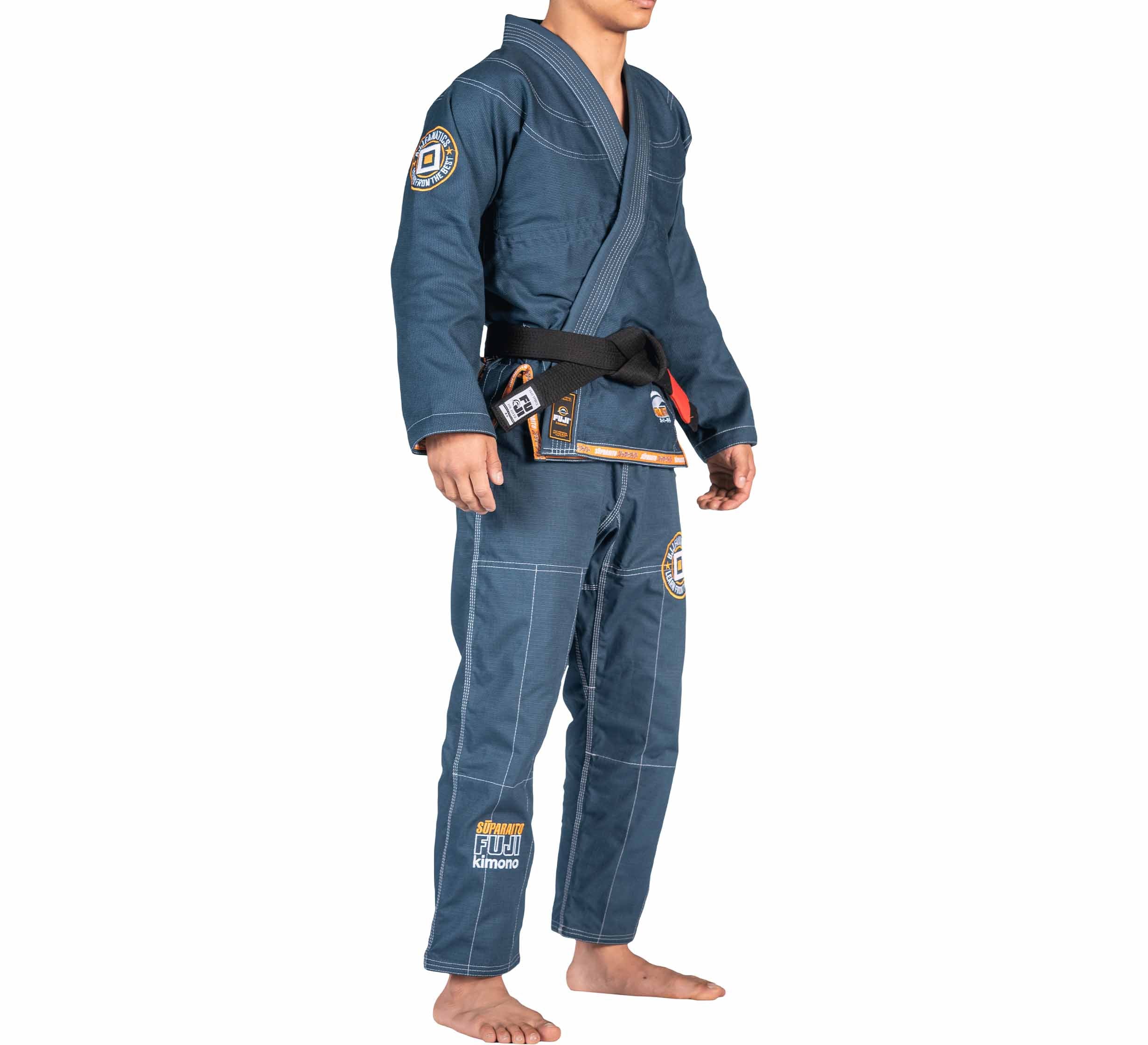 A person stands barefoot against a white background wearing the FUJI X BJJ Fanatics Blue Suparaito Gi, featuring visible stitching, embroidered logos on the chest, arms, and legs, and is paired with a black belt.