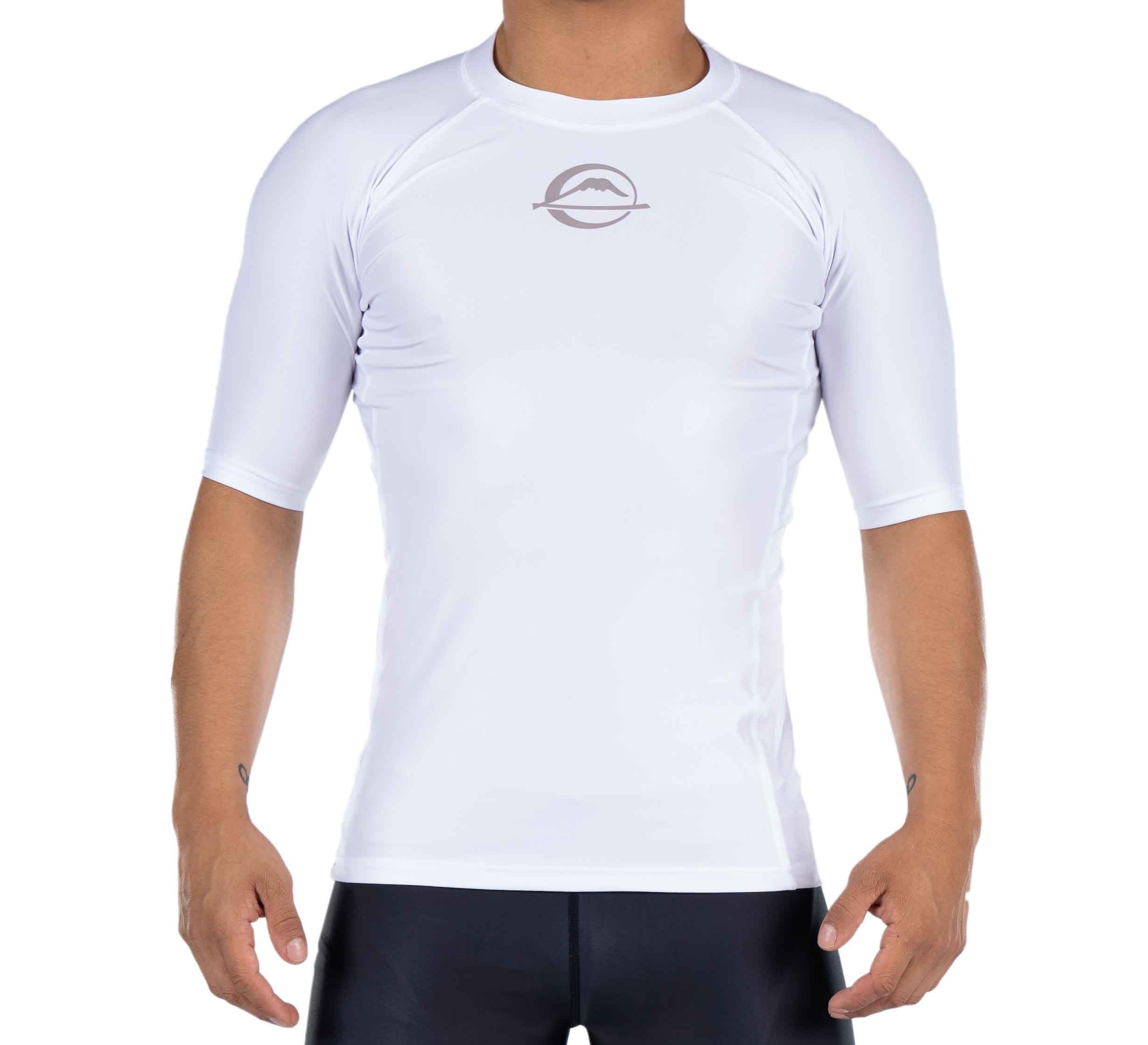 A person wears the Baseline Ranked Short Sleeve Rashguard, a fitted white athletic shirt with a small round chest logo, paired with black shorts, standing against a plain white background.