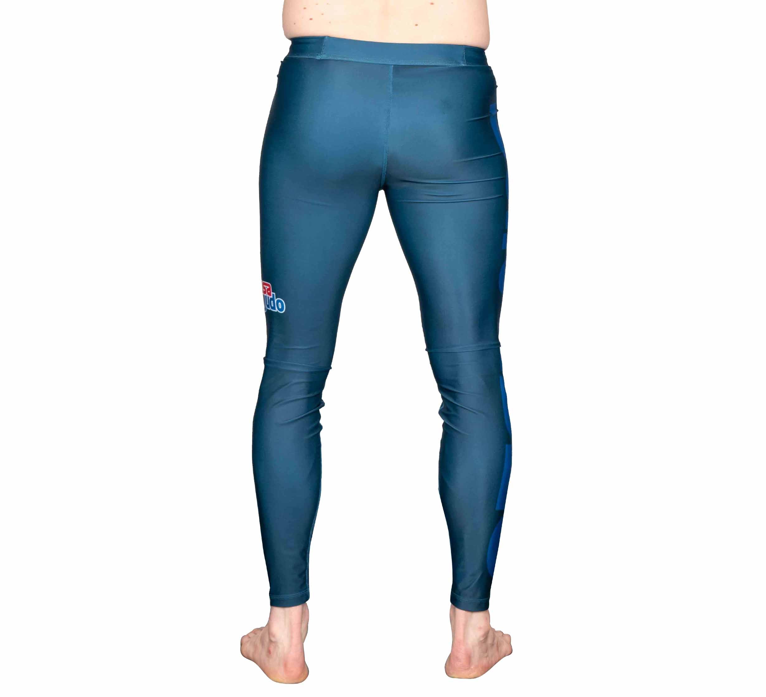 A person stands barefoot facing away from the camera, wearing shiny USA Judo Spats Blue leggings with a small red and white logo on the upper right side, against a white background.