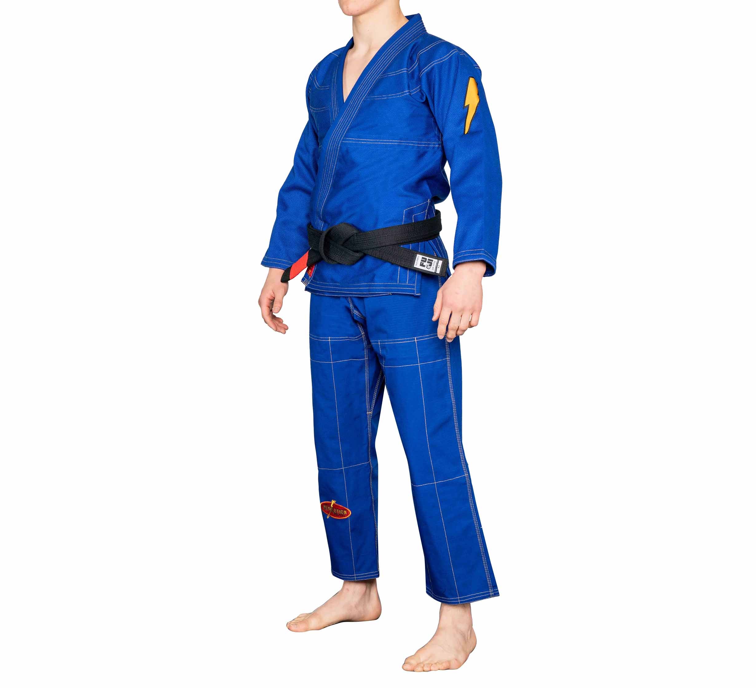 A person wearing the BJJ Revolution Warrior Gi in blue with a black belt stands barefoot on a white background. The gi features a lightning bolt patch on the left shoulder and reinforced stitching.