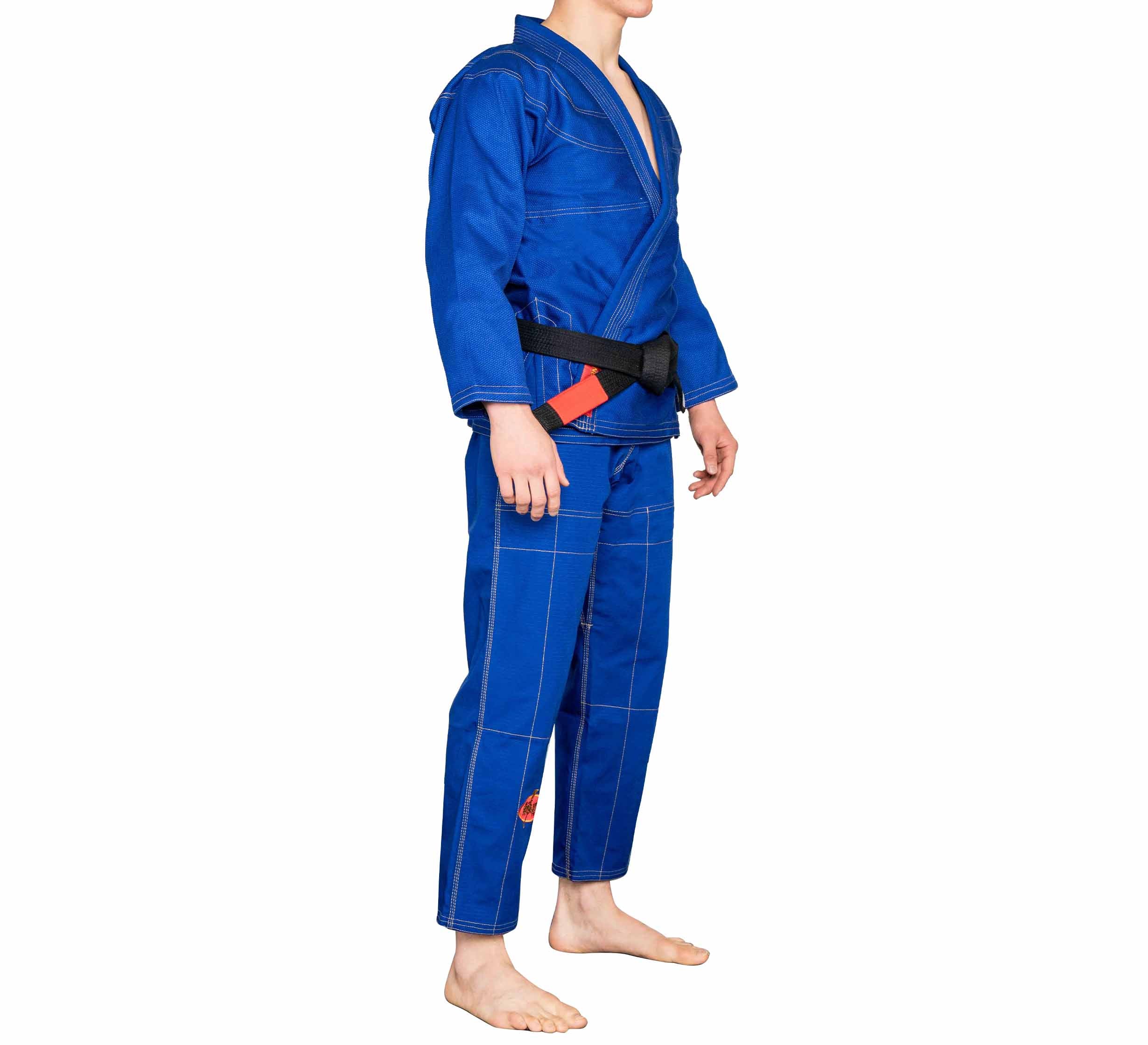 A person in the BJJ Revolution Warrior Gi with a black belt stands barefoot on a white background, facing slightly left. The blue gi features visible stitching and a red patch on the left pant leg.
