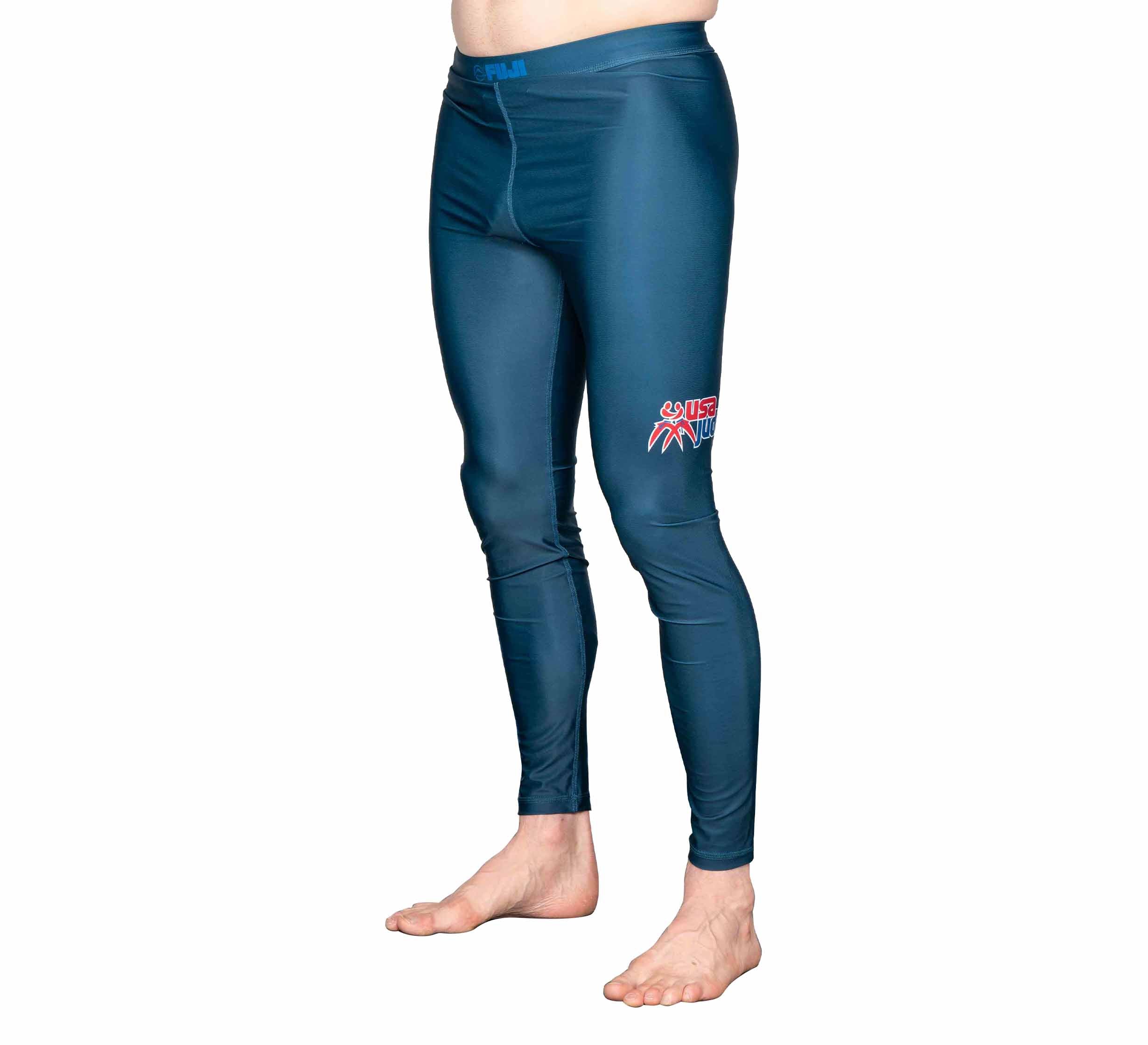 A person is barefoot and standing against a white background, wearing USA Judo Spats Blue featuring a small red and white logo on the left thigh.