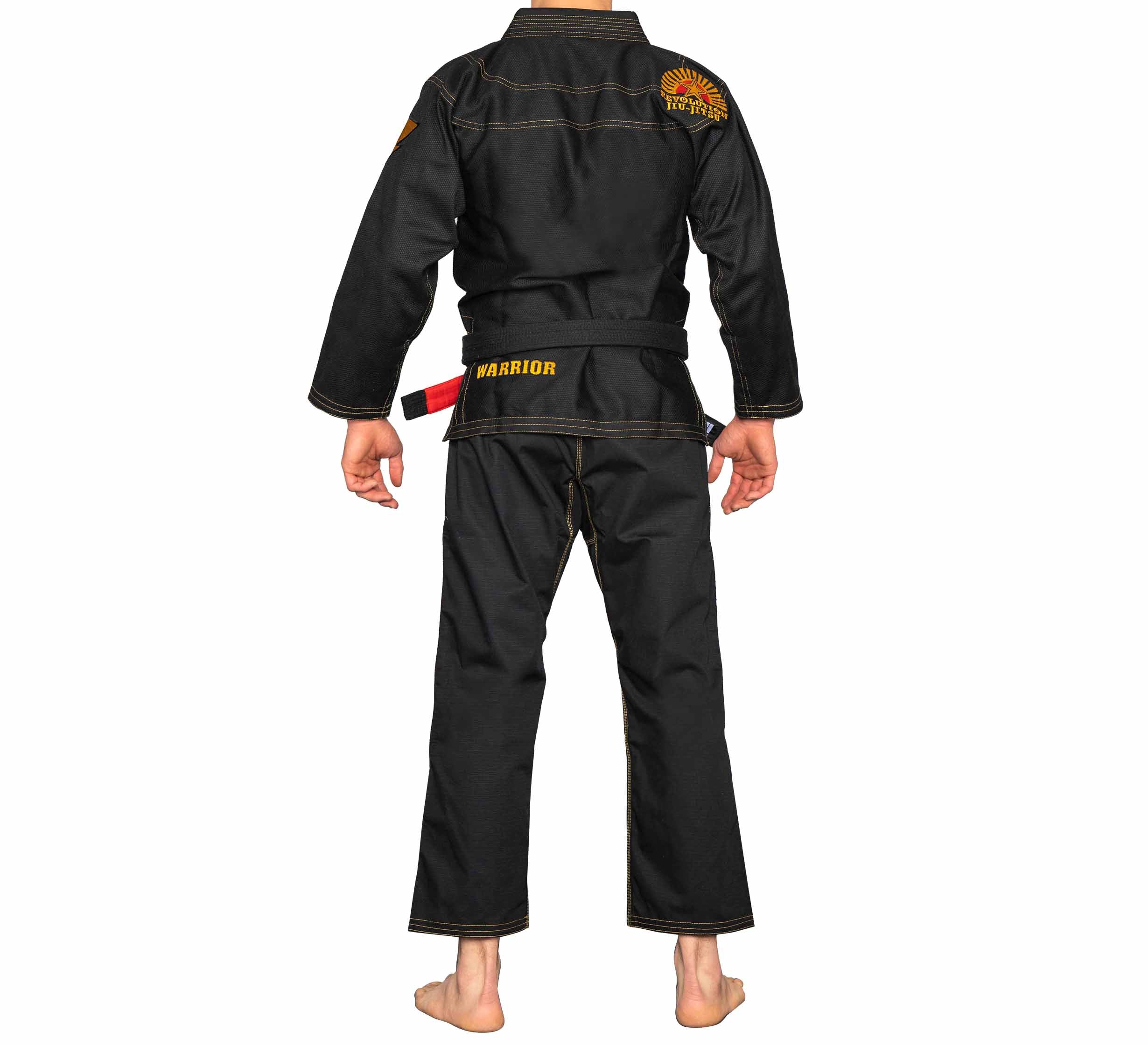 A person stands barefoot, back to camera, wearing the black BJJ Revolution Warrior Gi with yellow stitching, "WARRIOR" on the belt and back, and a sun patch with text on the shoulder.