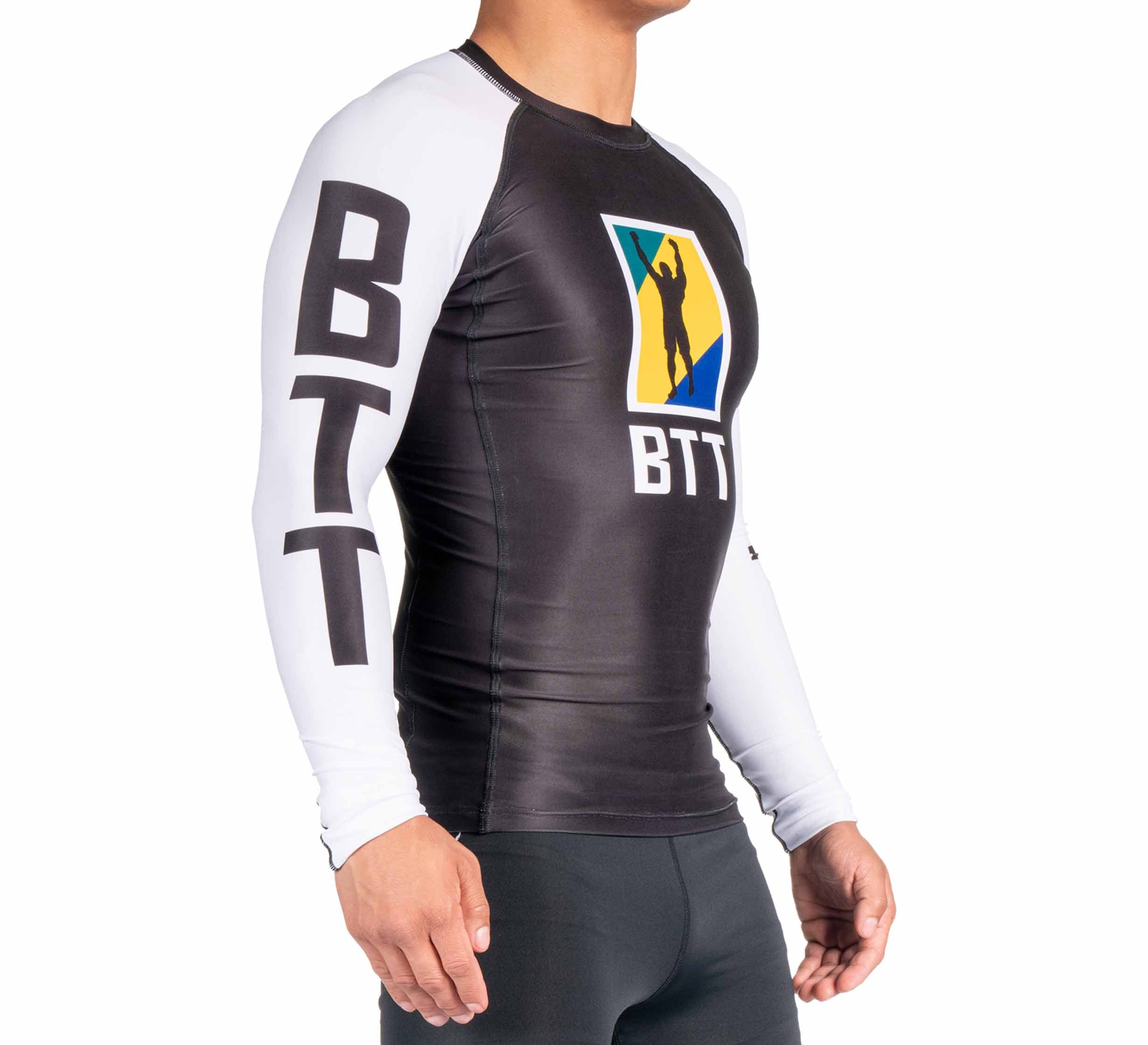A person wearing the BTT Ranked Long Sleeve Rashguard (NEW), featuring black and white colors, BTT text on the sleeve, and a colorful silhouette logo on the chest, stands against a white background.