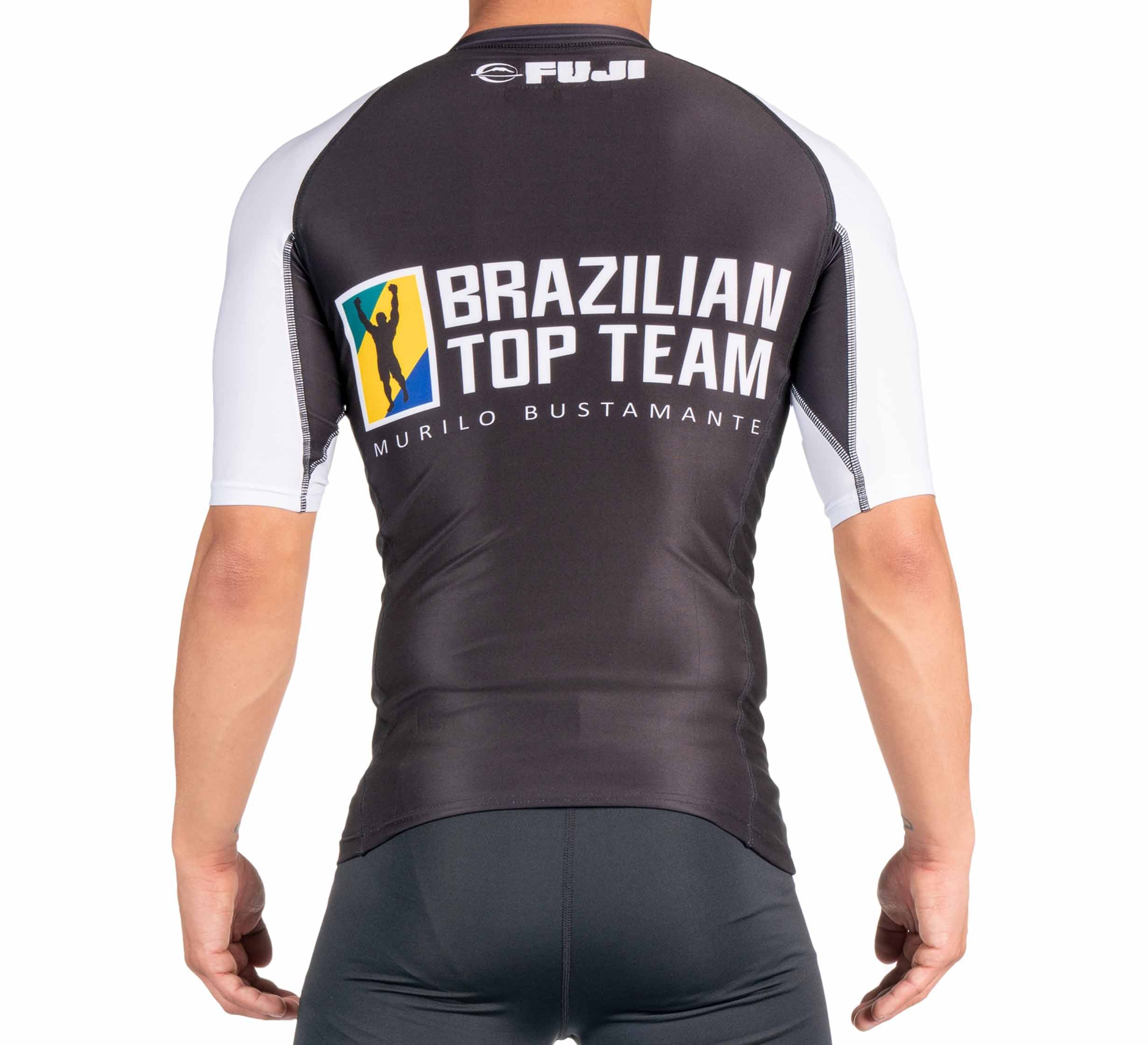 A person wearing the BTT Ranked Short Sleeve Rashguard (NEW) in black and white, seen from the back, with "Brazilian Top Team Murilo Bustamante" and "Fuji" logos on the upper back.