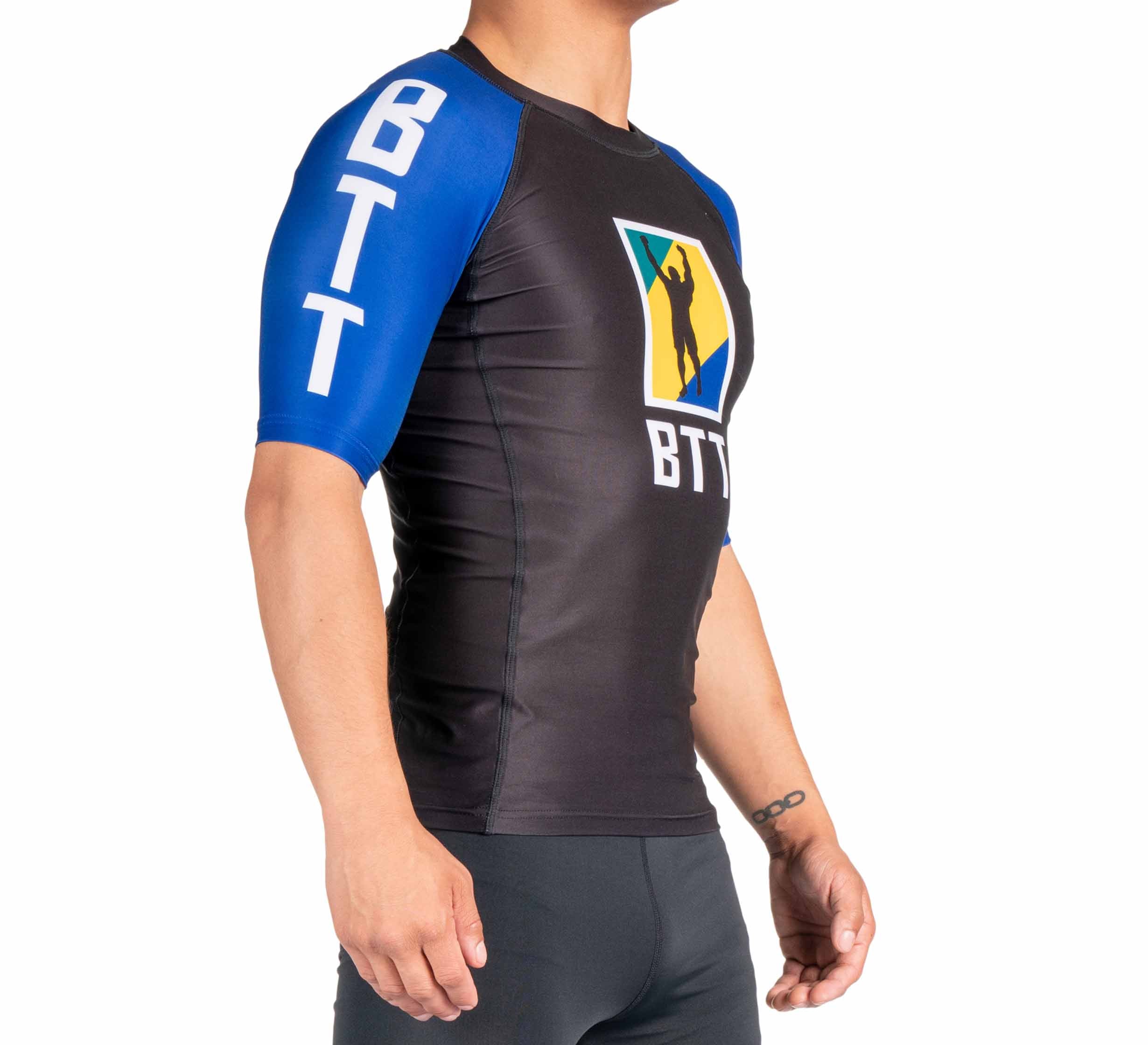 A person wearing the BTT Ranked Short Sleeve Rashguard (NEW), black and blue with "BTT" on the sleeve and chest, and a colorful logo showing a silhouette raising one arm.