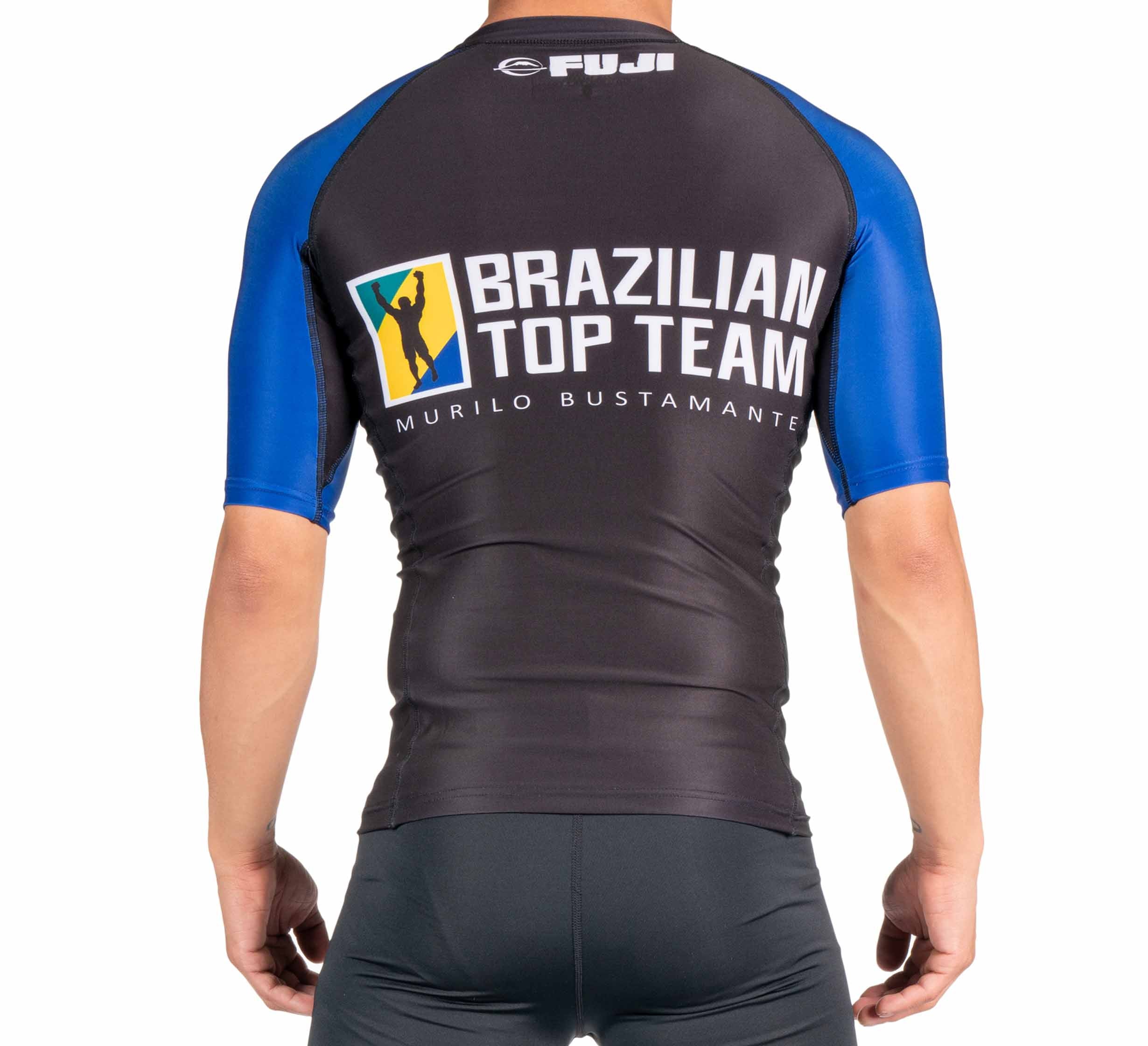 A person seen from the back is wearing the BTT Ranked Short Sleeve Rashguard (NEW) in black and blue, featuring white Brazilian Top Team Murilo Bustamante and Fuji logos.