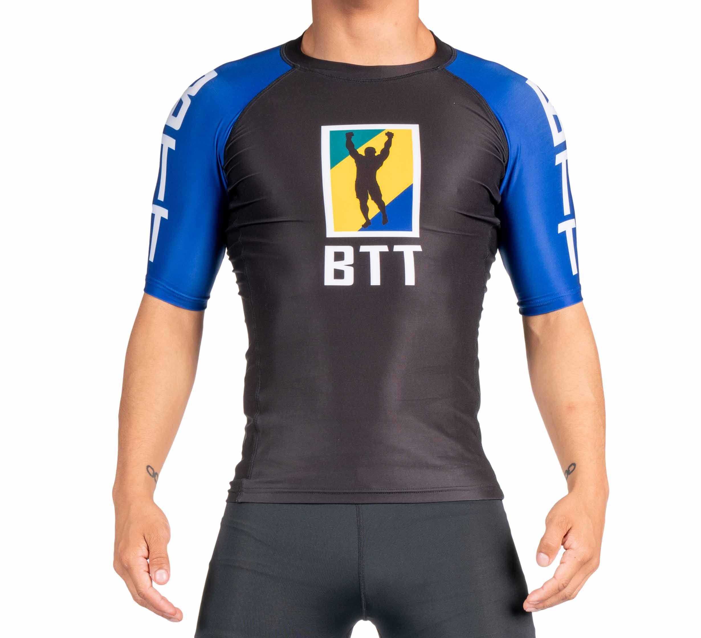A person wearing the BTT Ranked Short Sleeve Rashguard (NEW) in black and blue with BTT and a silhouette logo on the front stands against a plain white background, with their head cropped out of the image.