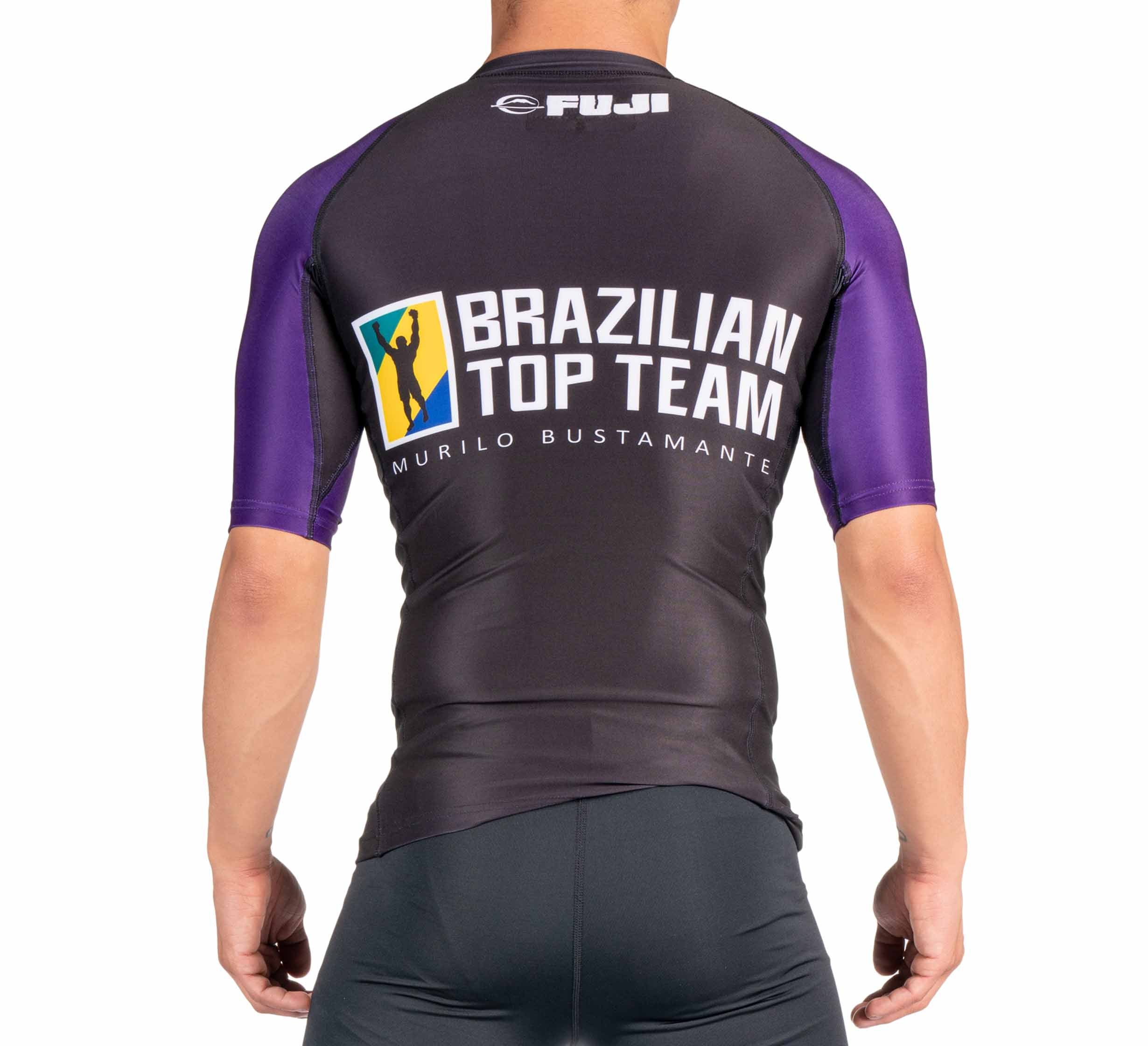 A person wearing the BTT Ranked Short Sleeve Rashguard (NEW), black and purple with “Brazilian Top Team Murilo Bustamante” and the FUJI logo on the back, photographed from behind.