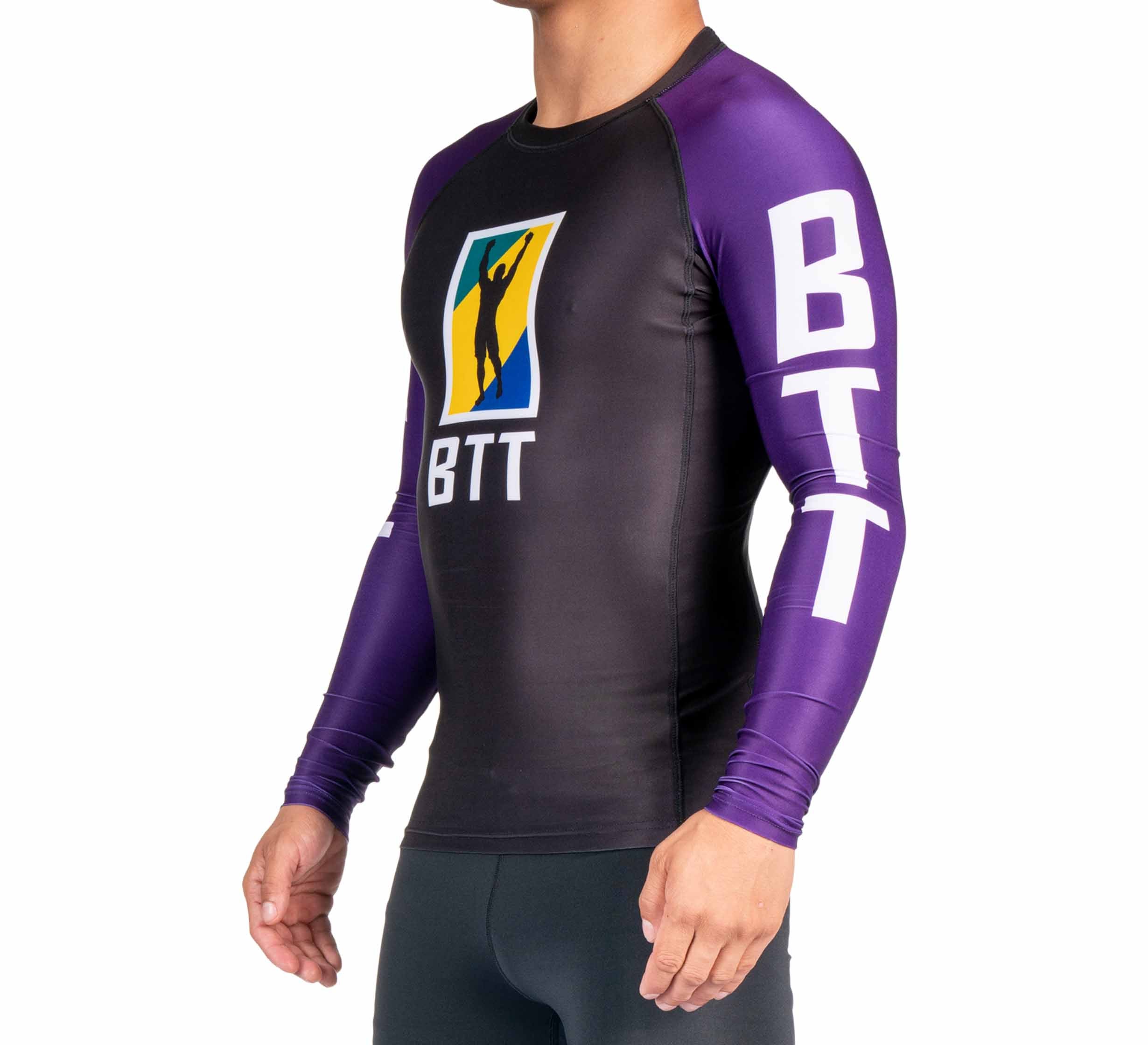 A person wears the BTT Ranked Long Sleeve Rashguard (NEW) in purple and black, featuring "BTT" on the sleeves and chest and a colorful rectangular logo on the front. The person's head is not shown.