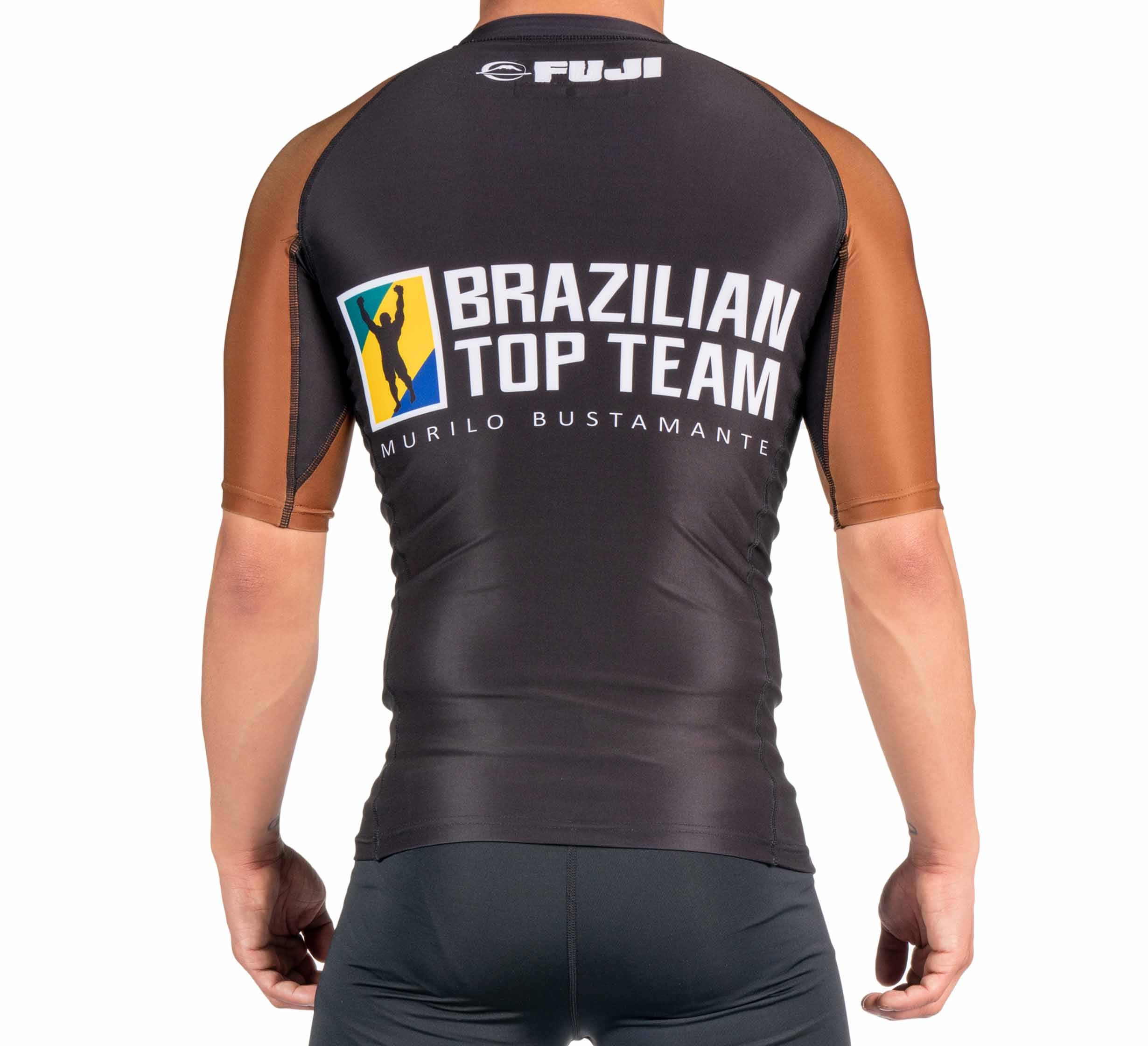 A person is wearing the BTT Ranked Short Sleeve Rashguard (NEW), featuring black and brown colors, "Brazilian Top Team Murilo Bustamante" text, a logo on the back, and the Fuji brand visible near the collar.