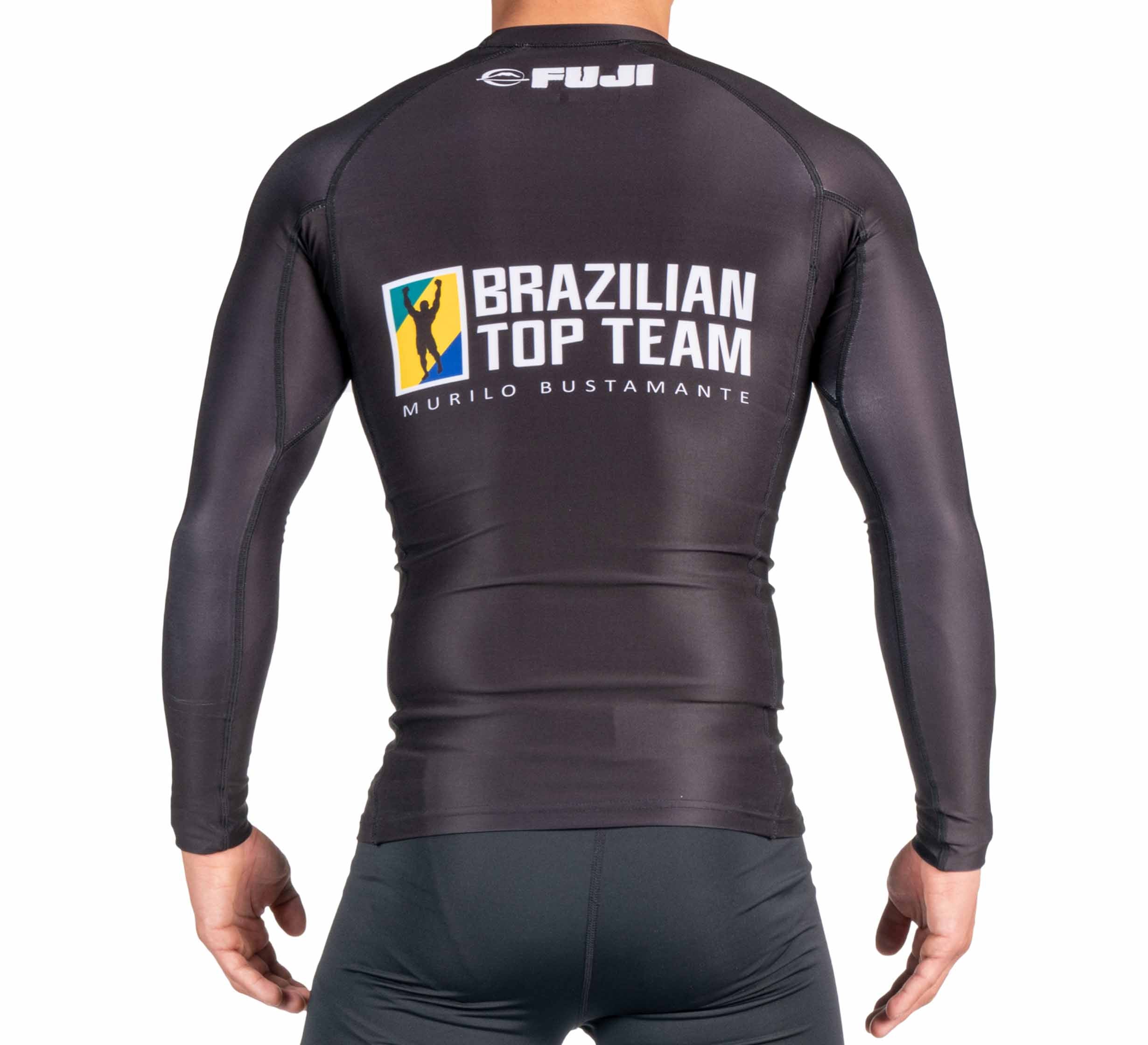 A person is facing away from the camera, wearing the BTT Ranked Long Sleeve Rashguard (NEW) in black, featuring Brazilian Top Team Murilo Bustamante and FUJI logos printed on the back.