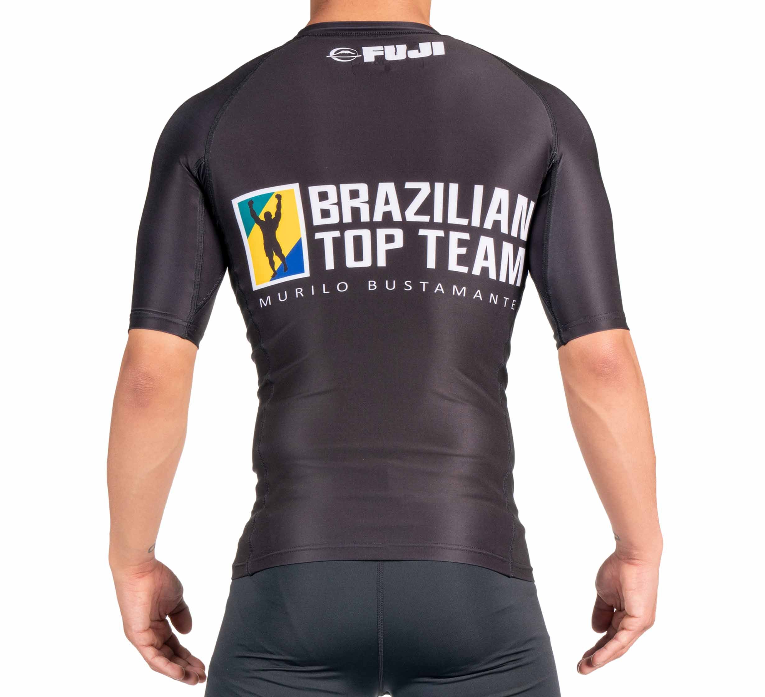 A person wears the BTT Ranked Short Sleeve Rashguard (NEW), a black athletic shirt featuring Brazilian Top Team Murilo Bustamante design and logo on the back, with Fuji branding at the top.