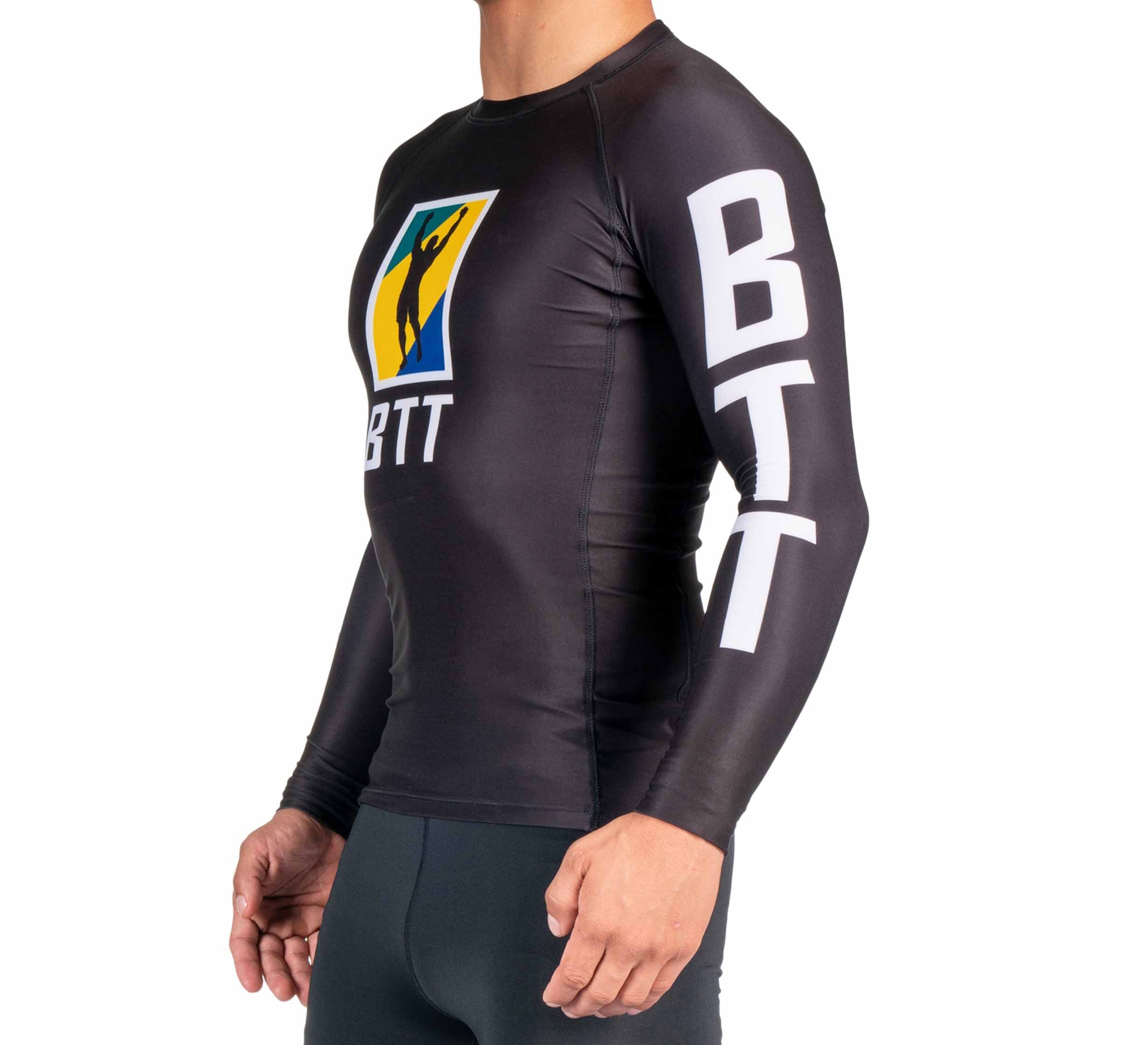 A person wears the BTT Ranked Long Sleeve Rashguard (NEW): a black athletic top with bold white "BTT" on the arm and chest, plus a colorful logo on the chest, standing against a plain white background.
