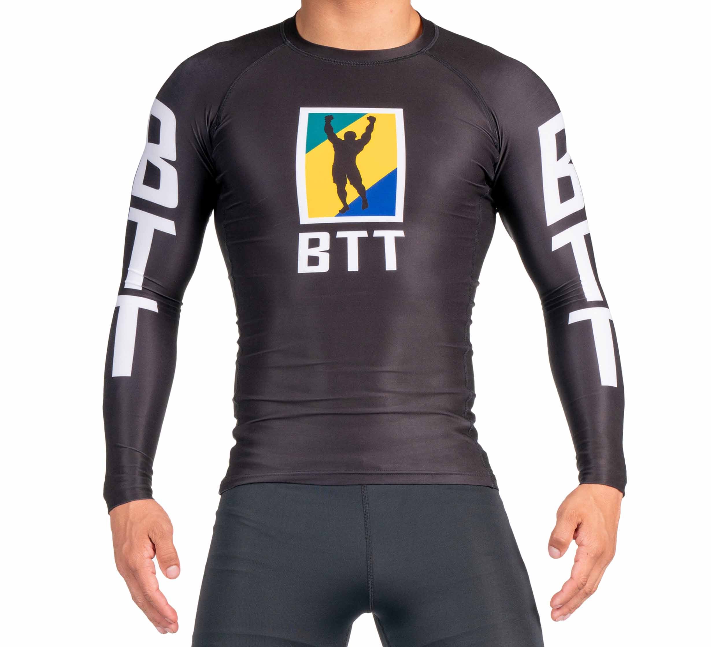 A person wearing the BTT Ranked Long Sleeve Rashguard (NEW), a fitted black top featuring "BTT" in white on the sleeves and chest, plus a logo of a figure raising an arm before a yellow, green, and blue background.