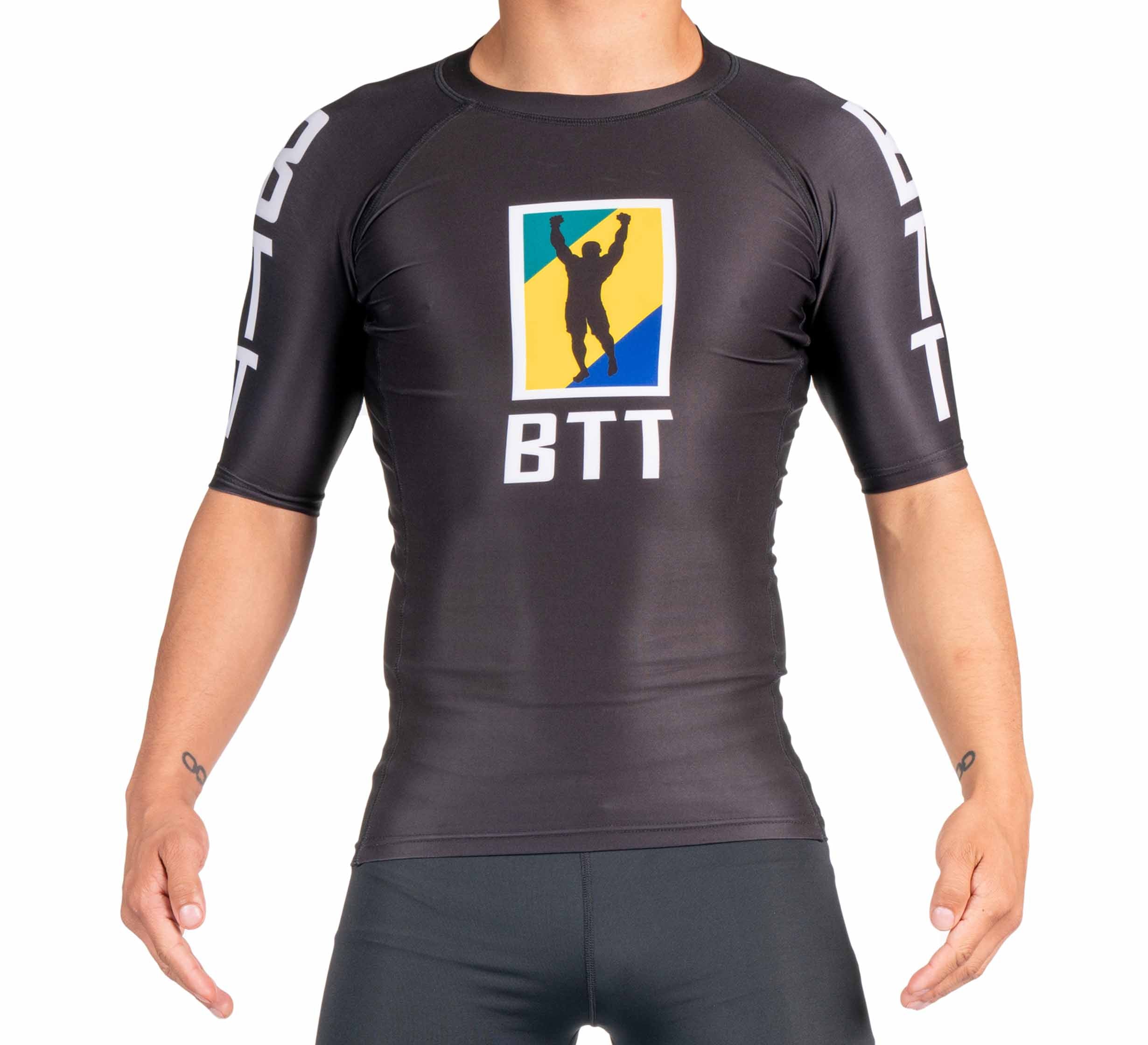 A person models the BTT Ranked Short Sleeve Rashguard (NEW), a fitted black athletic top with BTT lettering on the chest and sleeves, plus a colorful logo featuring a silhouette of a raised-arm figure. The person's head is not visible.