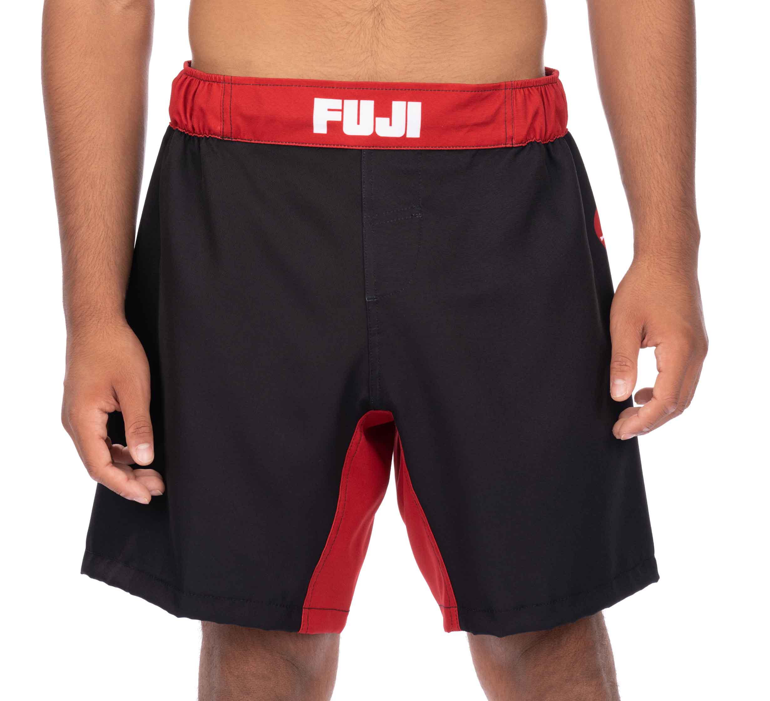 A person wearing Essential Grappling Red Fight Shorts with black and red color and "FUJI" written in white on the waistband, shown from waist to mid-thigh.