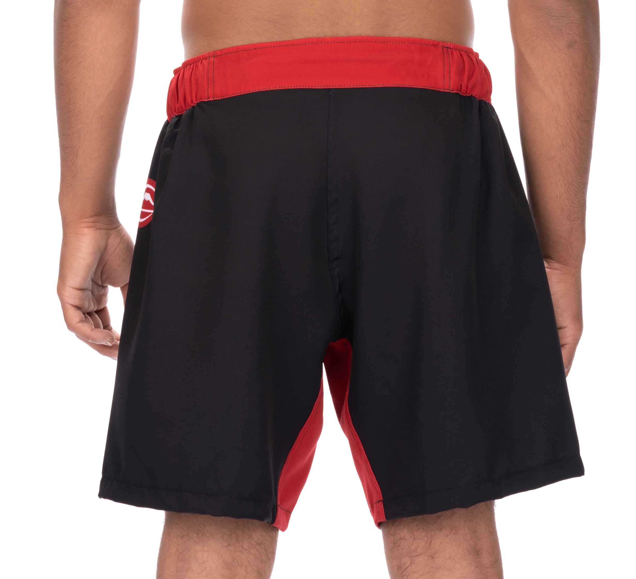 A person shown from the back wears Essential Grappling Red Fight Shorts, featuring black fabric with red accents and an elastic waistband. Their hands are relaxed at their sides.