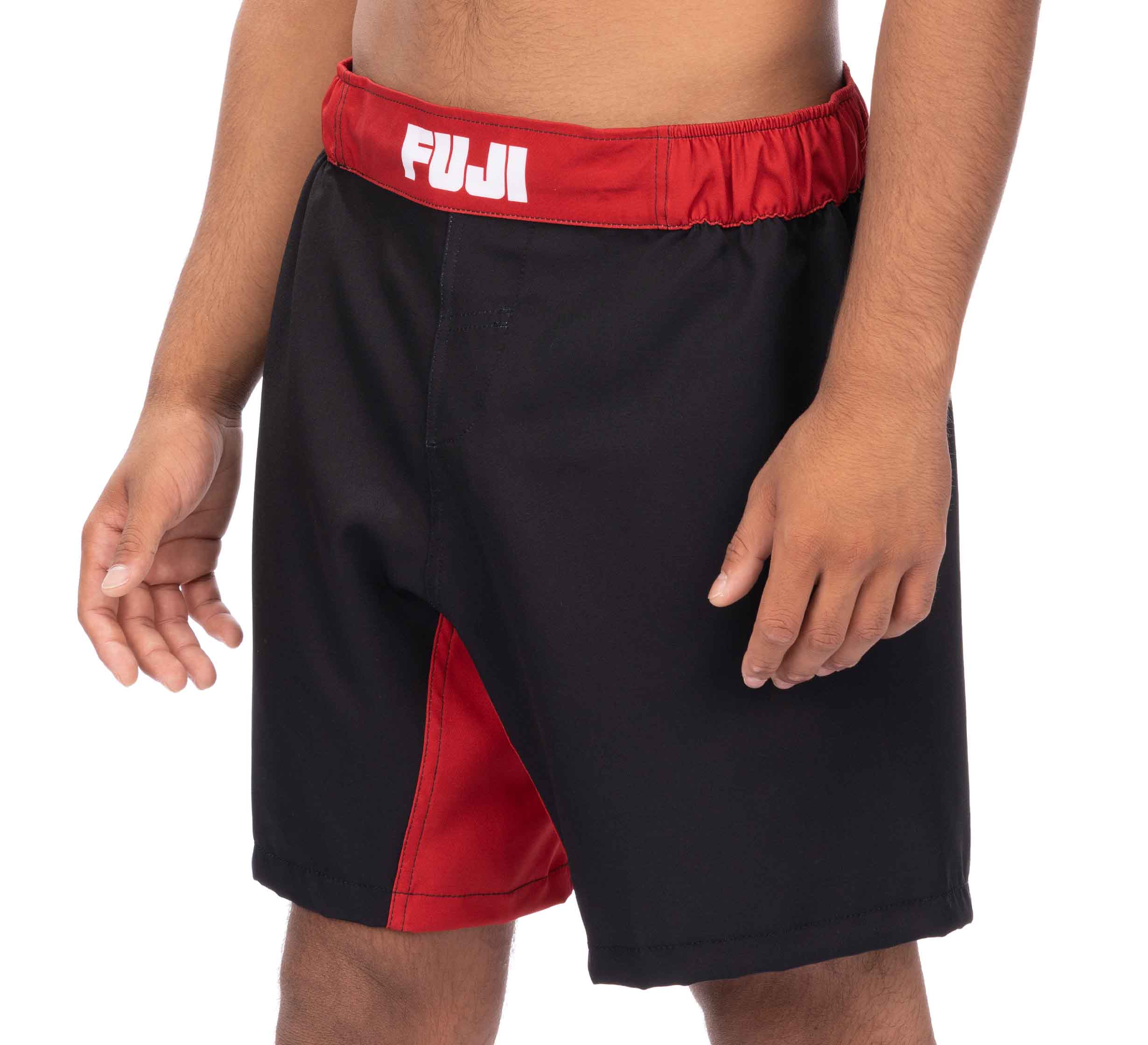 A person wears Essential Grappling Red Fight Shorts, featuring black fabric, a red waistband and side panel, with "FUJI" in white on the waistband. Only the torso and upper legs are shown.