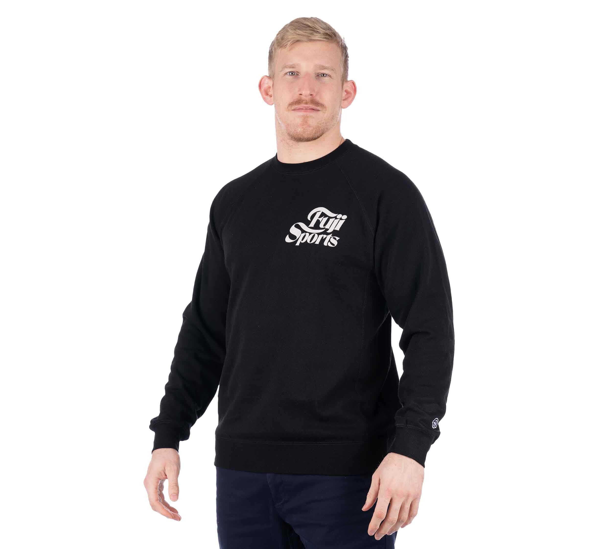 A man with short blond hair and a mustache is wearing a black Wave Crewneck Men's Sweatshirt and dark pants, standing slightly turned to the right against a plain white background.